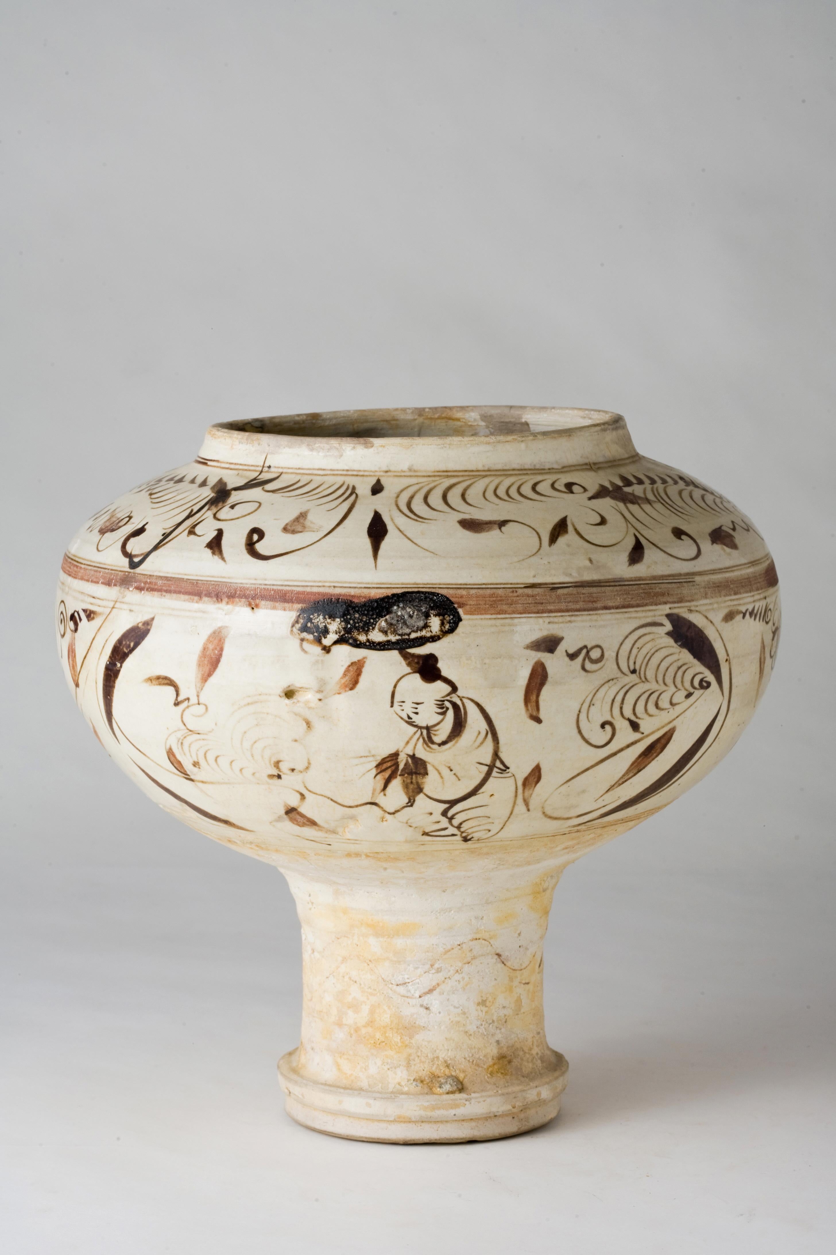 The vase features a broad, rounded body with a slightly flared neck and a pedestal base. The decoration consists of intricate brushwork in iron-brown pigment, depicting figures and swirling motifs that are typical of the Cizhou style. The glaze has