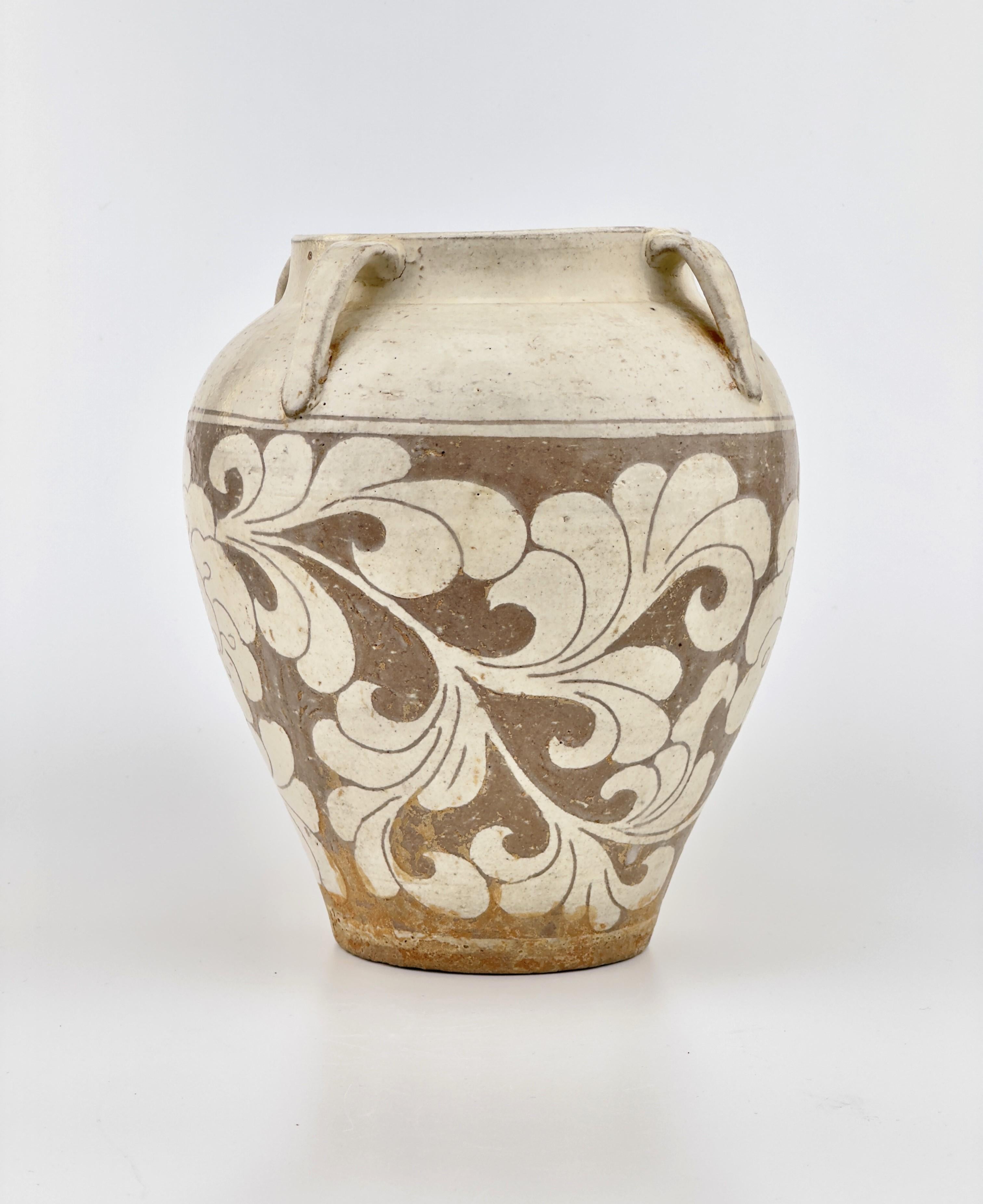 Dieses Gefäß weist ein geschnitztes Muster auf, das typisch für Cizhou-Ware ist. Es hat eine cremeweiße und braune Farbgebung und die auffällige Dekoration der Lotusblume, die ein häufiges Motiv in der chinesischen Kunst und Kultur ist und Reinheit