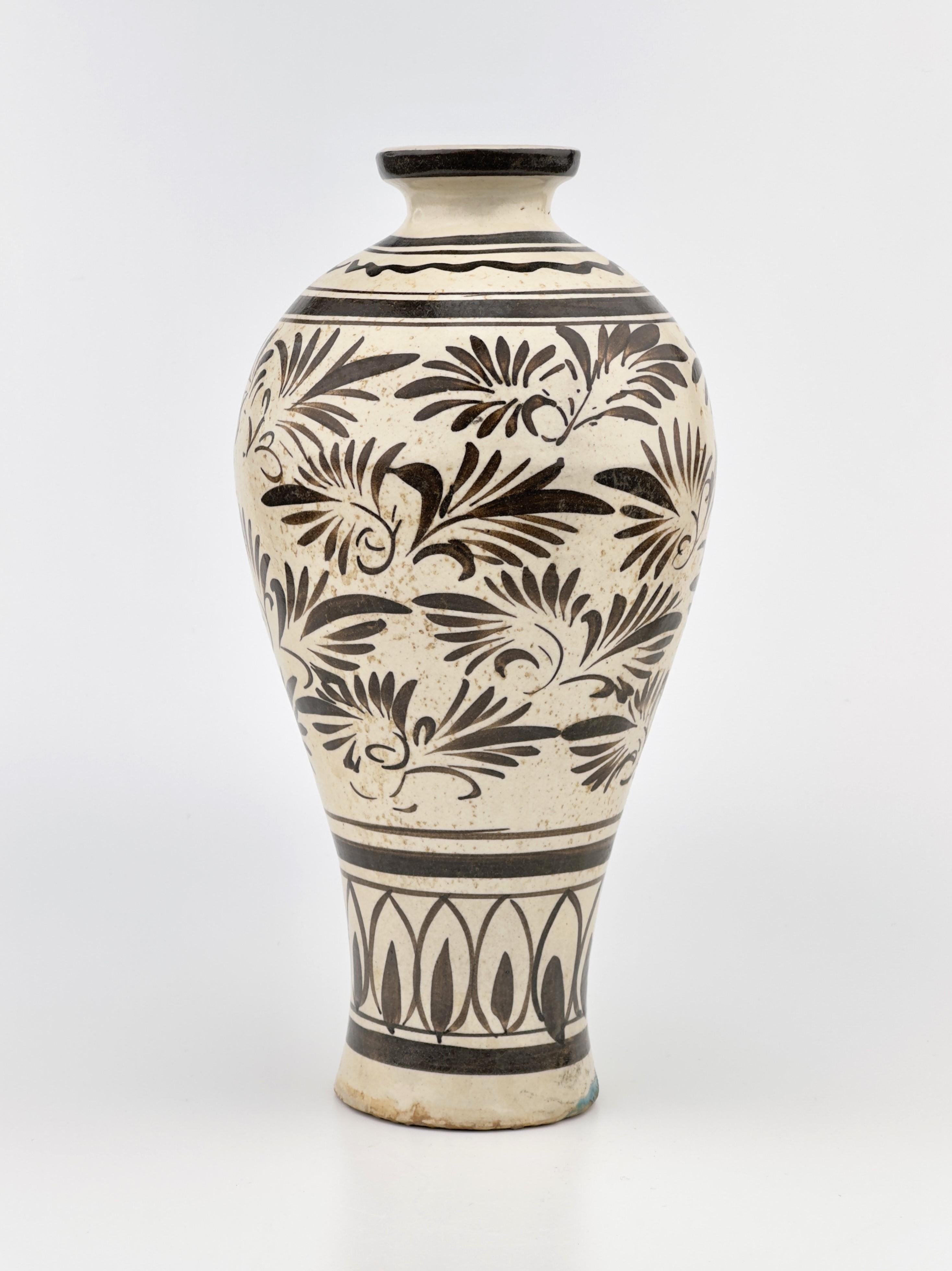The elongated body is fluidly painted in brown on a white slip and under a clear glaze with a broad band of abstract floral scroll between a band of upright petals below and further chain-like decoration on the shoulder.

Period : Yuan