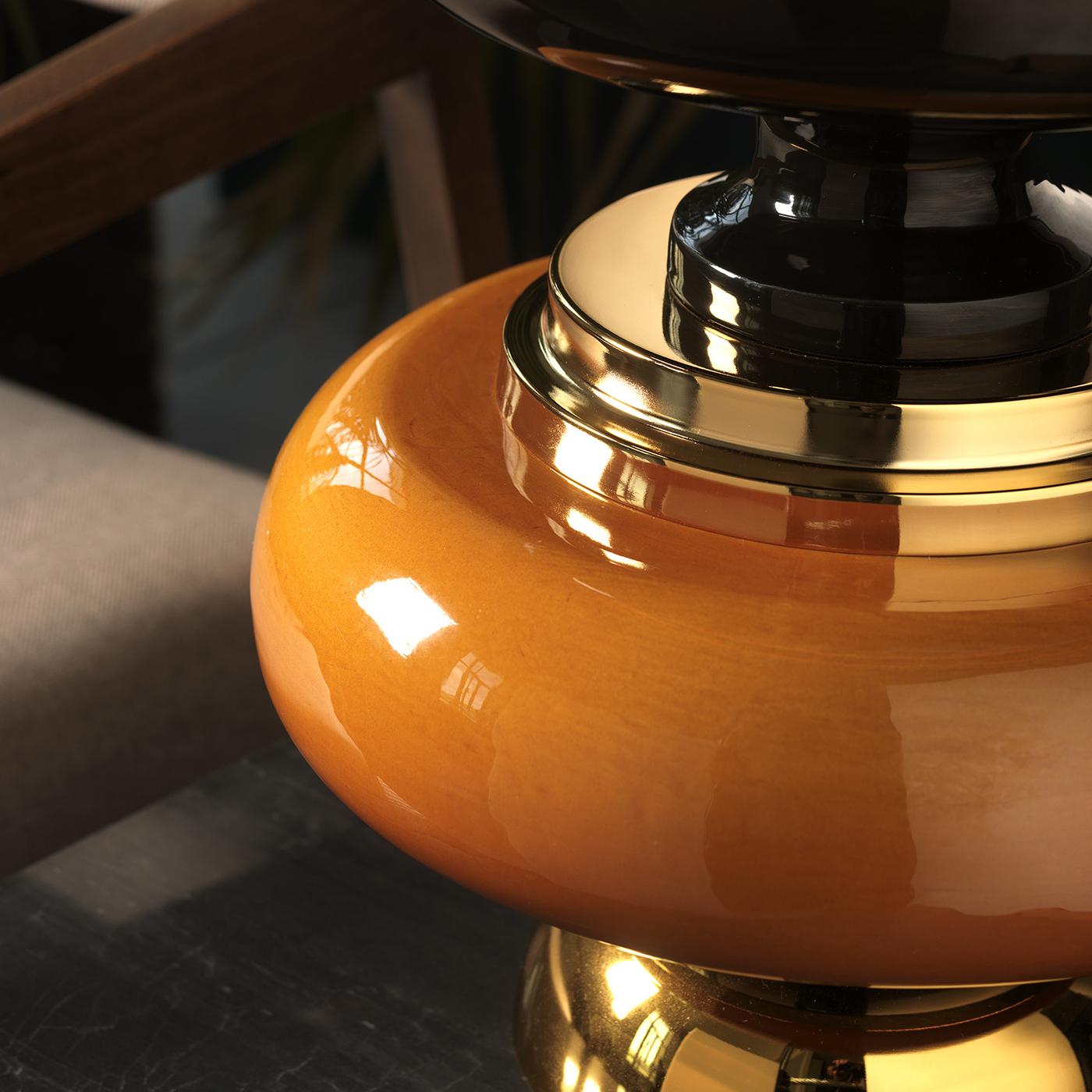 This short table lamp features a dynamic play on horizontal shapes and lines. Along with the light's illumination, its black, gold and amber colors add warmth and depth. It is topped by a unique double shade with an exterior layer in black chintz
