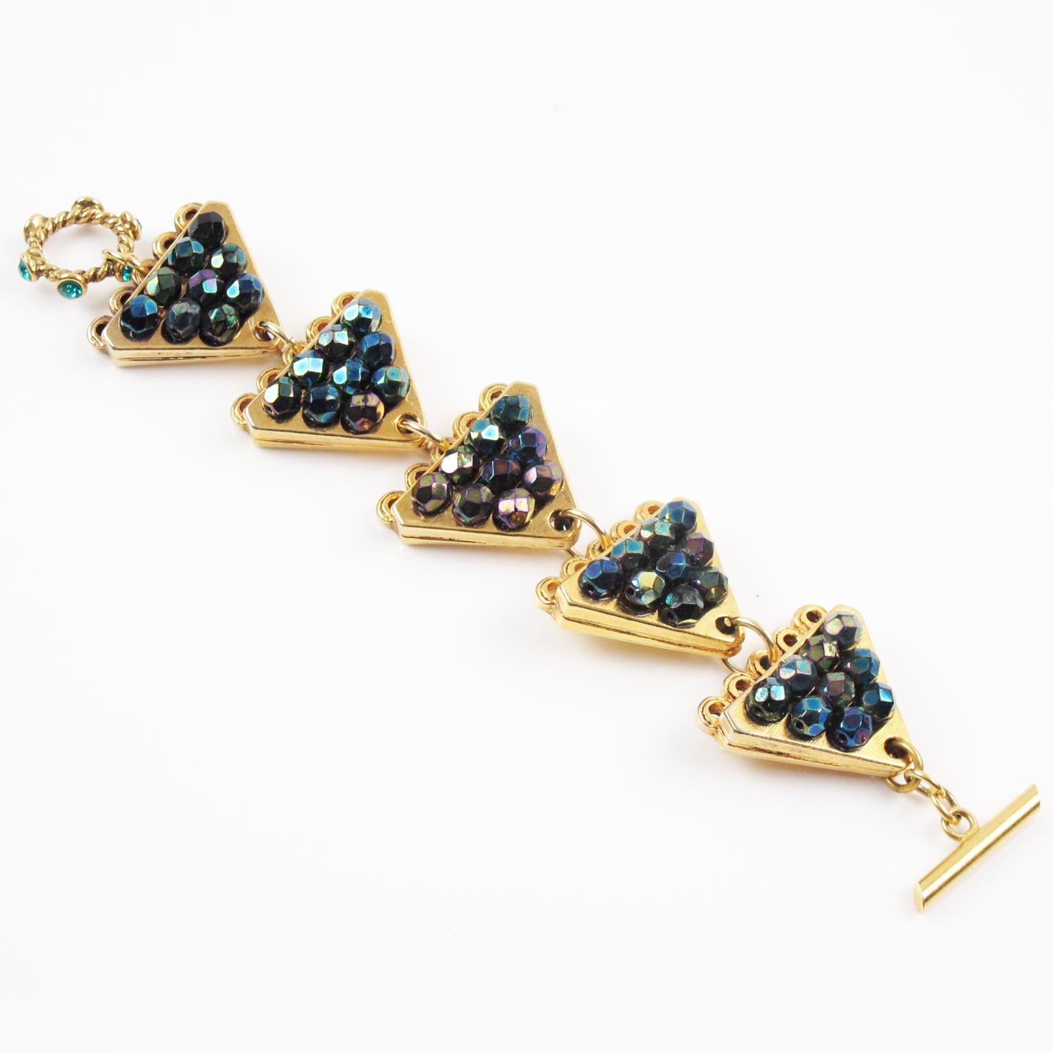 This lovely Claire Deve Paris signed link bracelet features a geometric shape with triangle gilt metal elements paved with faceted crystal beads in assorted purple and green iridescent colors. There is a jeweled toggle closing clasp with turquoise