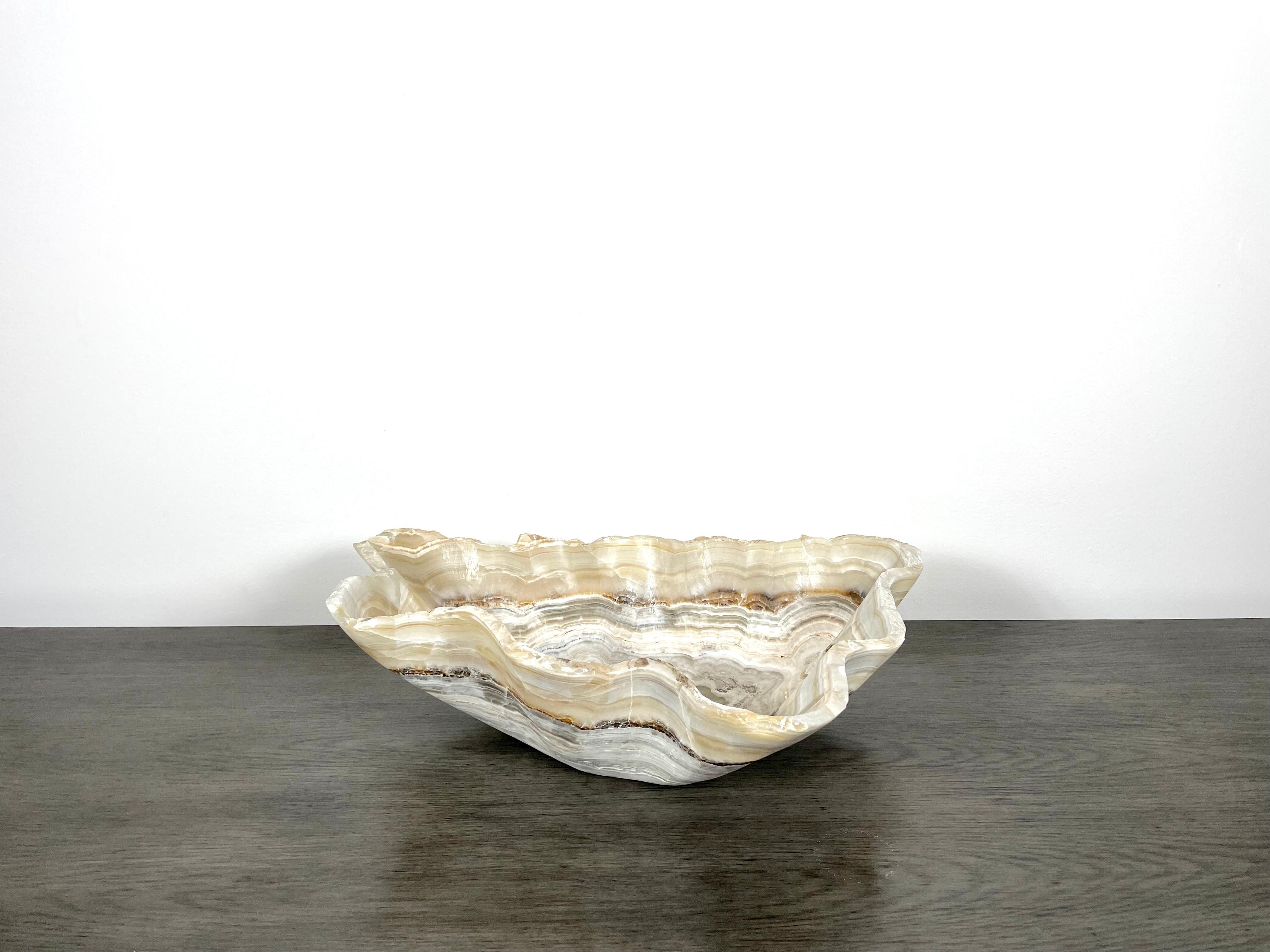 An exquisite medium onyx bowl with a raw edge. This bowl has tones of cream, beige and grey, with thin dark rust-colored veining. This one of a kind decorative bowl is meticulously hand-carved from a single piece of onyx by skilled artists to reveal