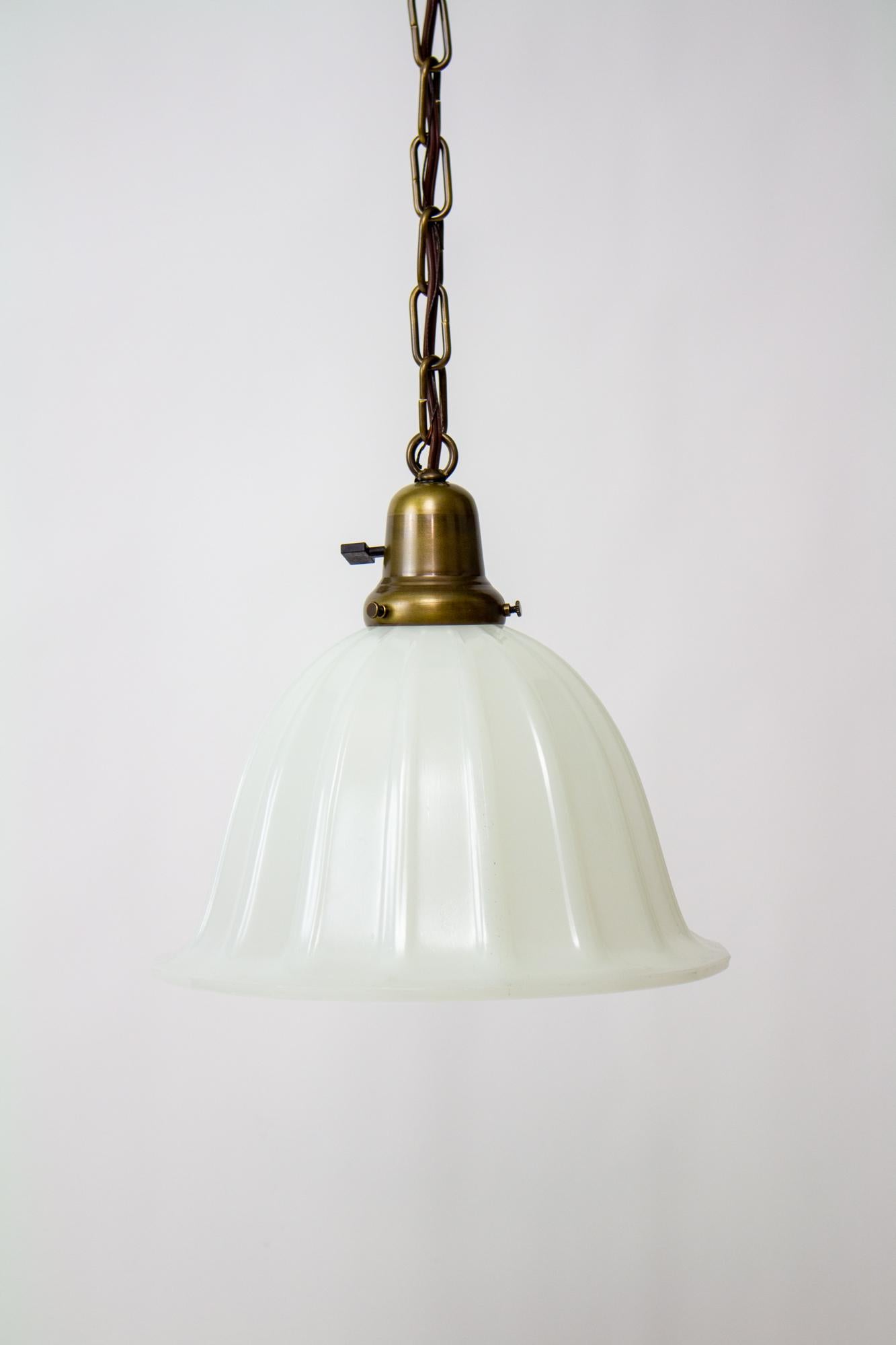 Early 20th Century clambroth glass bell pendant light. Classic brass chain fixture with a single socket. Glass is thick and cast in a bell shape with ribs, it has an opaline translucency, less opaque than milk glass, and with a smooth finish. Glass