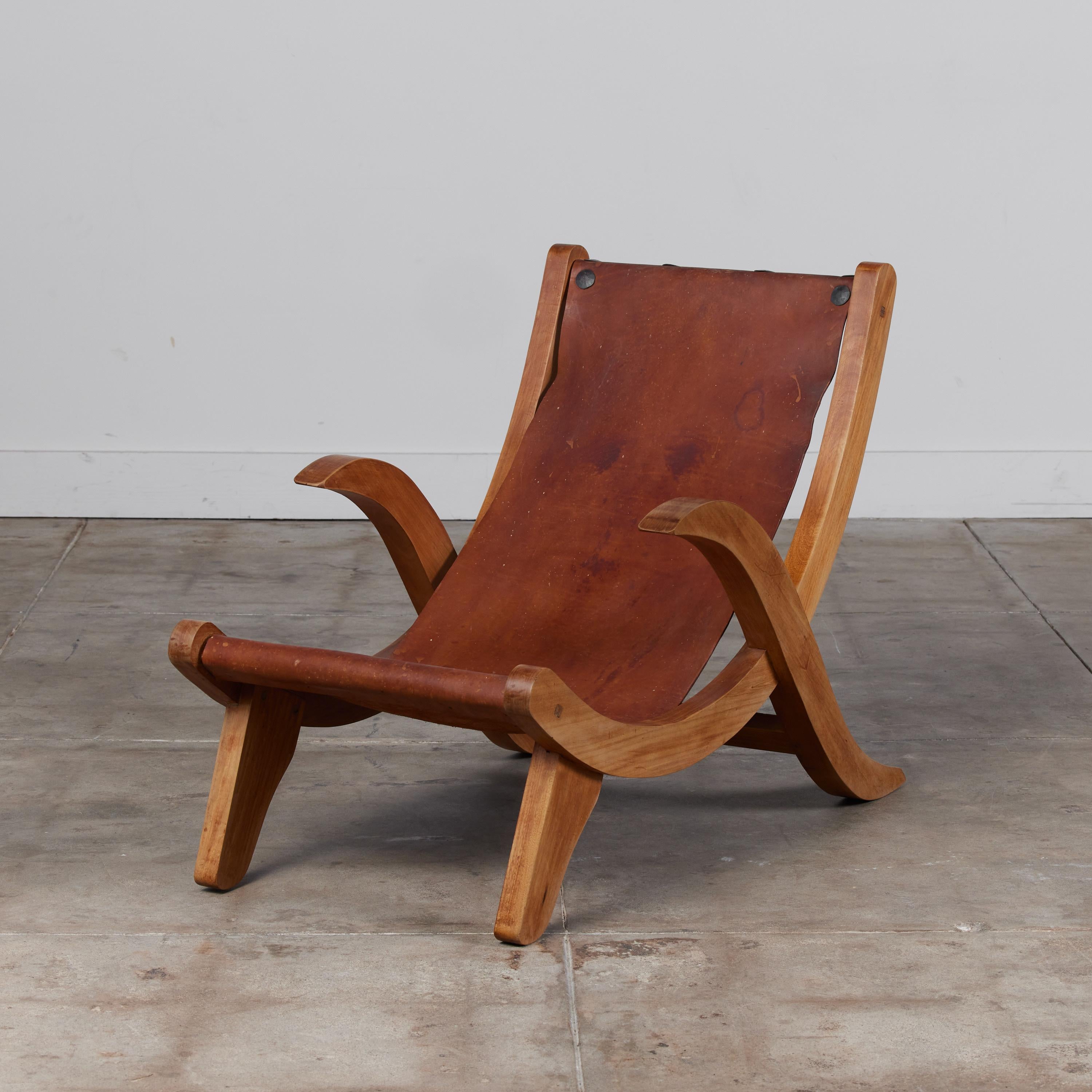 Clara Porset style butaque chair c.1970s, Mexico. The lounge chair features a curvaceous solid mahogany frame with the original brown saddle leather sling seat. The leather is wrapped around the frame and attached with patinated steel