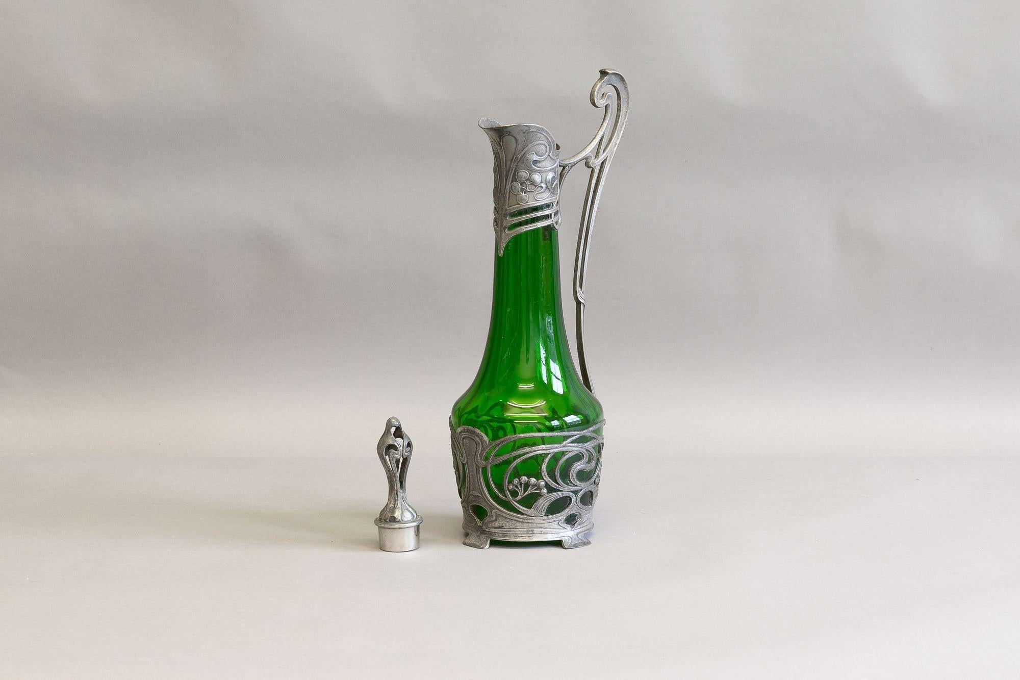Jarra de clarete de vidrio verde con asa y tapón decorativos de metal. Alrededor de 1900

Alto 36 cm x Ancho 11 cm x Fondo 18 cm