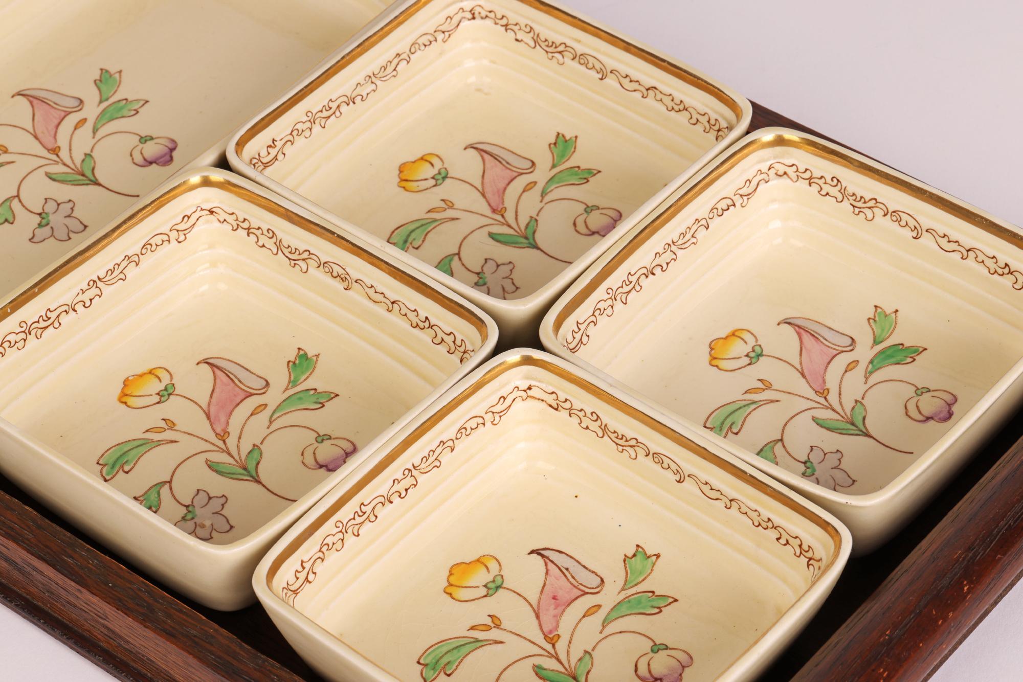 A stylish Art Deco pottery hors d’oeuvres floral painted dish set on an oak tray by Clarice Cliff (English, 1899-1972) and dating from the 1930’s. The dish set comprises of a larger rectangular shaped dish with raised sides with four matching