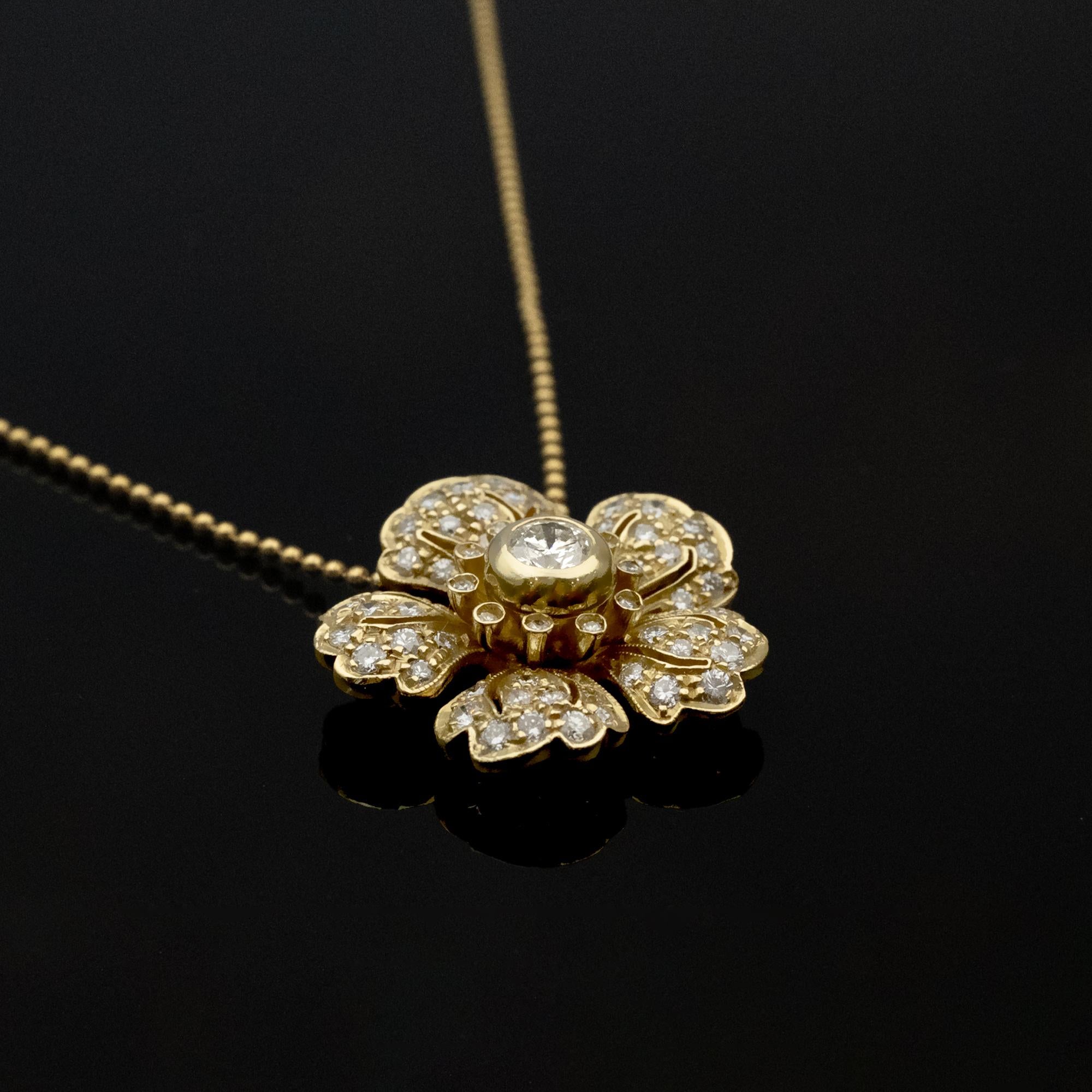 This refined pendant necklace is crafted in 18-karat yellow gold and designed as a stylized flower set with white diamonds. Each petal is delicately shaped and arranged to create a balanced, dimensional form. A larger diamond of approximately 0.35