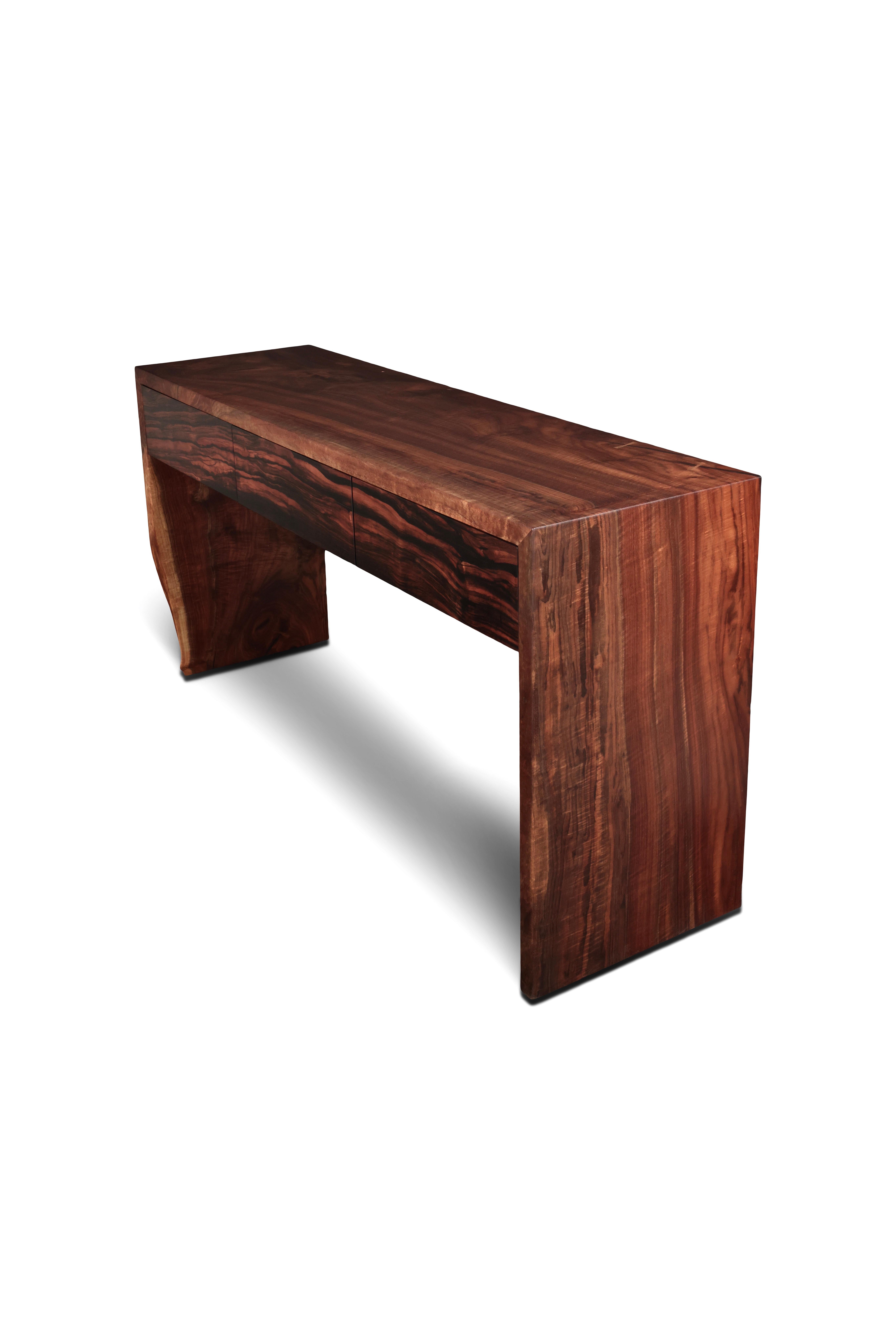 A single slab of figured Claro walnut creates a waterfall console table with an organic live edge detail down one leg. Beautifully contrasted with solid Macassar Ebony drawer fronts and solid Curly Maple, leather lined drawers. Exposed joinery and