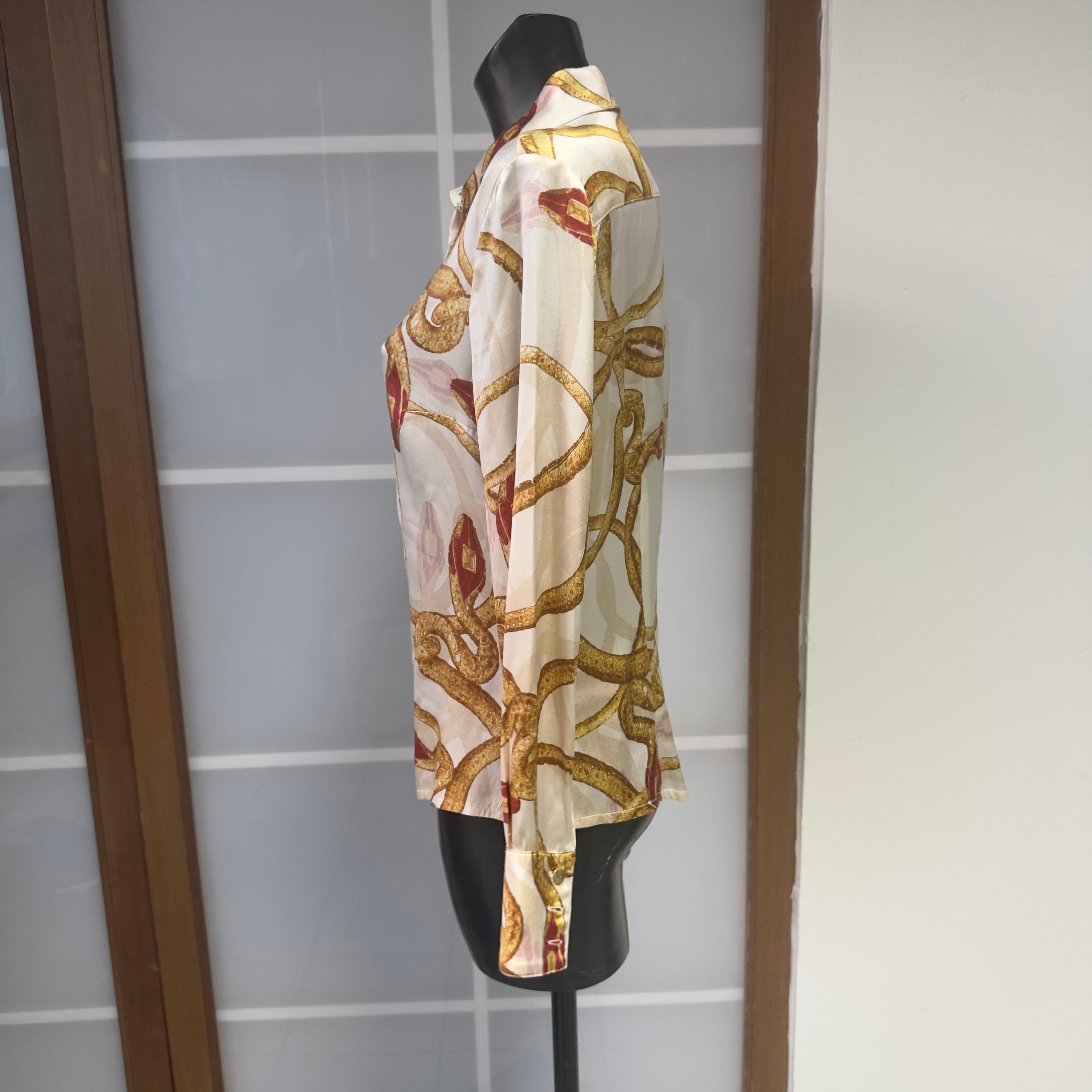 Una oda a la feminidad atrevida y sensual de Roberto Cavalli.
Esta lustrosa camisa de seda de la línea Class presenta un estampado de cadenas doradas sobre fondo marfil, embellecido con detalles en rojo rubí que recuerdan el mundo de la equitación