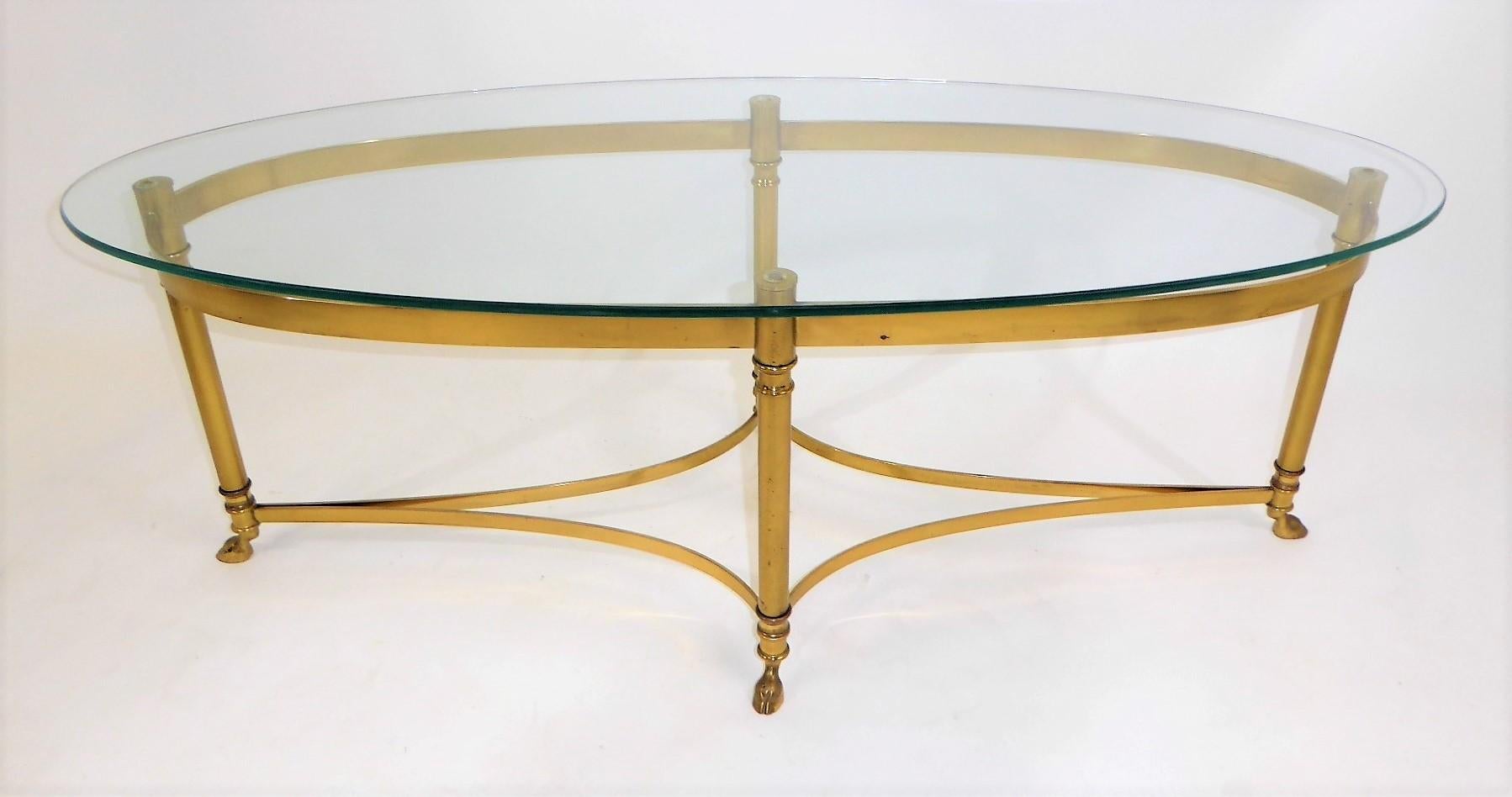Fine 1970s Labarge brass long oval coffee table featuring modern Hollywood Regency lines with Louis XVI styling with hooved feet and a new glass top. The styling reminding one of Maison Jansen table designs. The glass is new and the brass exhibits a