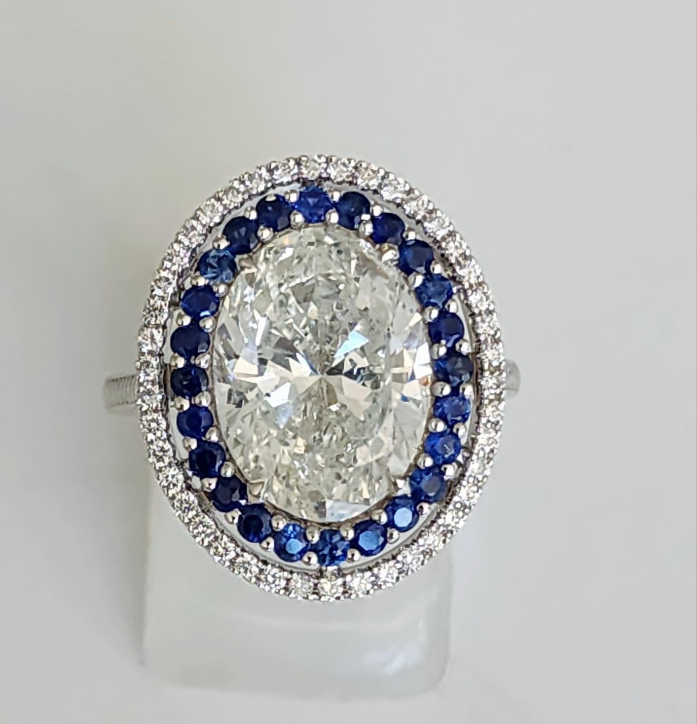 Magnificent 5.01 Carat Oval Diamond Ring with Sapphire and Diamond Halo. This exquisite ring features a dazzling 5.01 carat oval diamond at its heart, encircled by a double halo of vibrant blue sapphires and sparkling brilliant diamonds. The unique