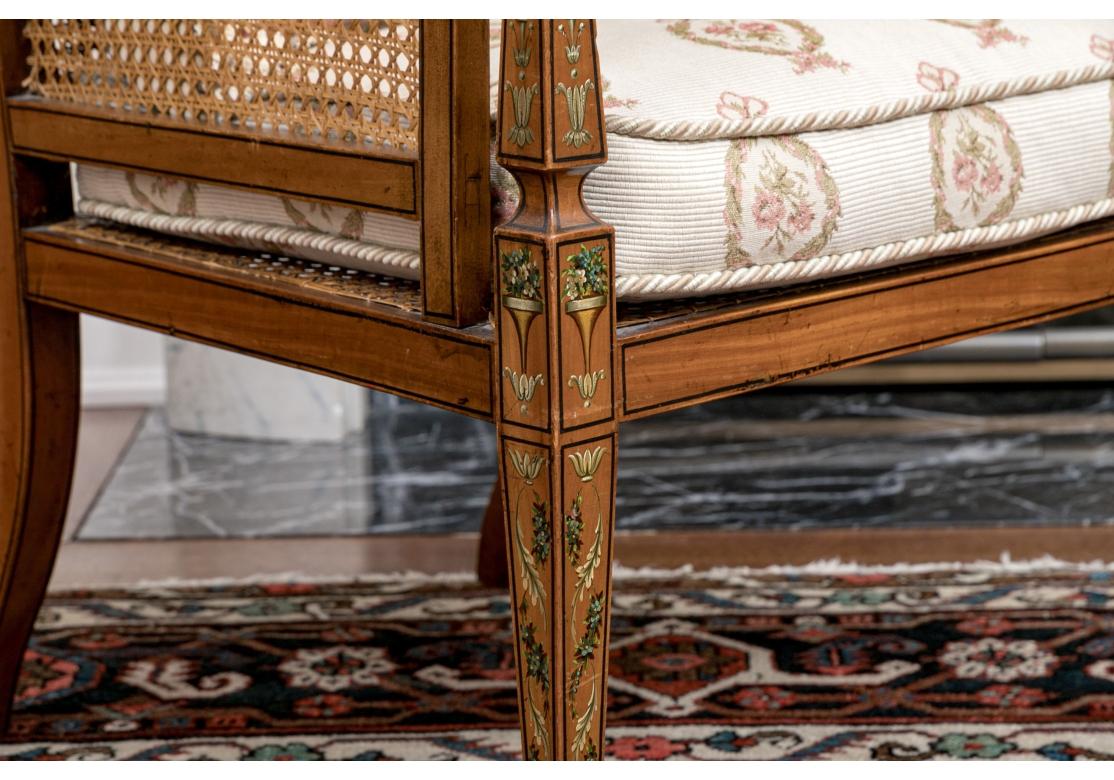 Un sillón muy fino con asiento, respaldo y laterales de caña tirada a mano. La silla tiene un armazón de madera de frutal con una cresta pintada que representa a tres querubines montados en nubes en tonos celadón y marfil, pintura de líneas negras