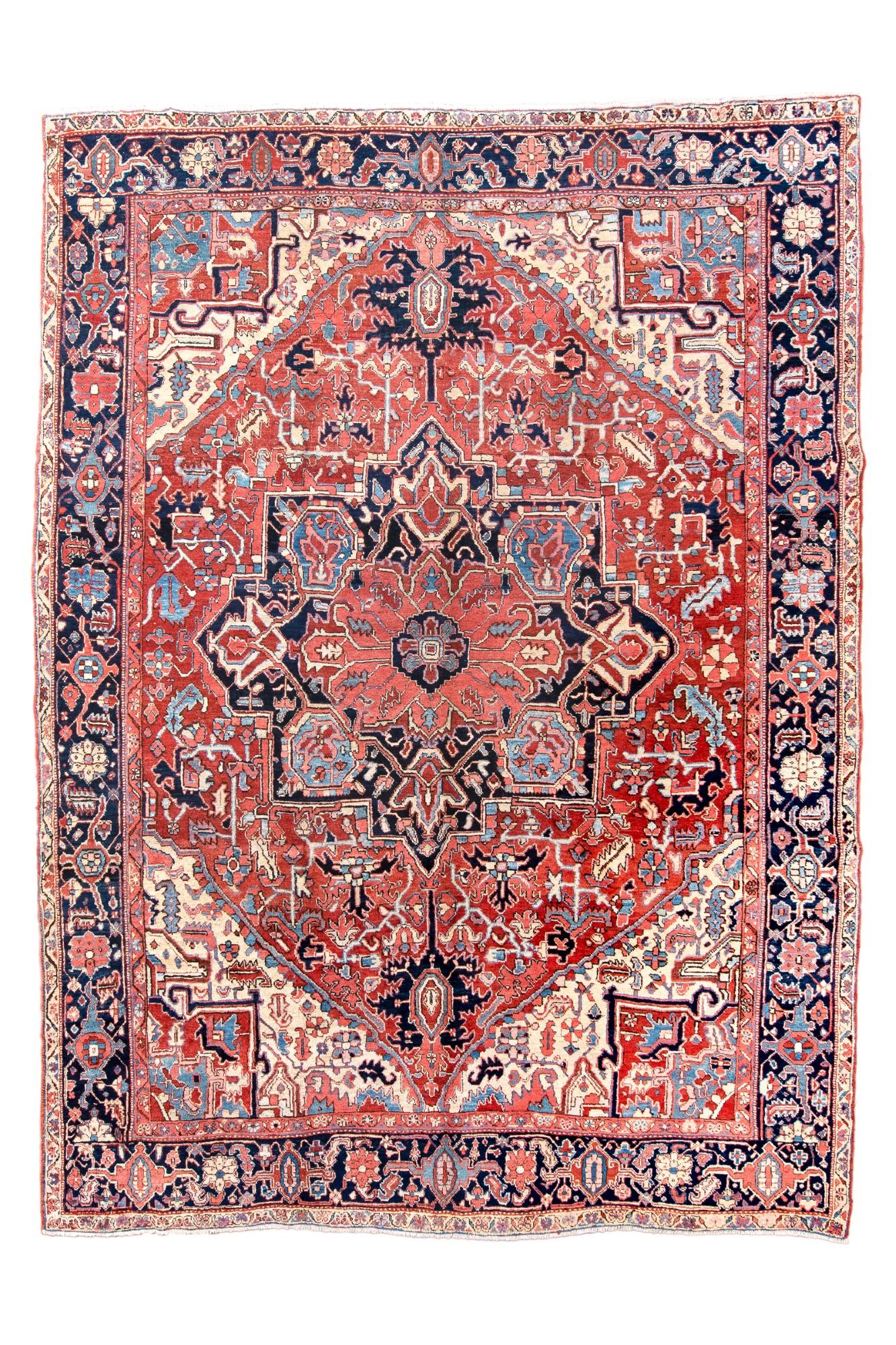 A rose sub-medallion is embedded in the larger navy octogramme medallion with ragged palmette pendants. The encompassing red field shows broken vinery and serrated leaves, set within ecru corners. Navy strip style main border with eccentric, long