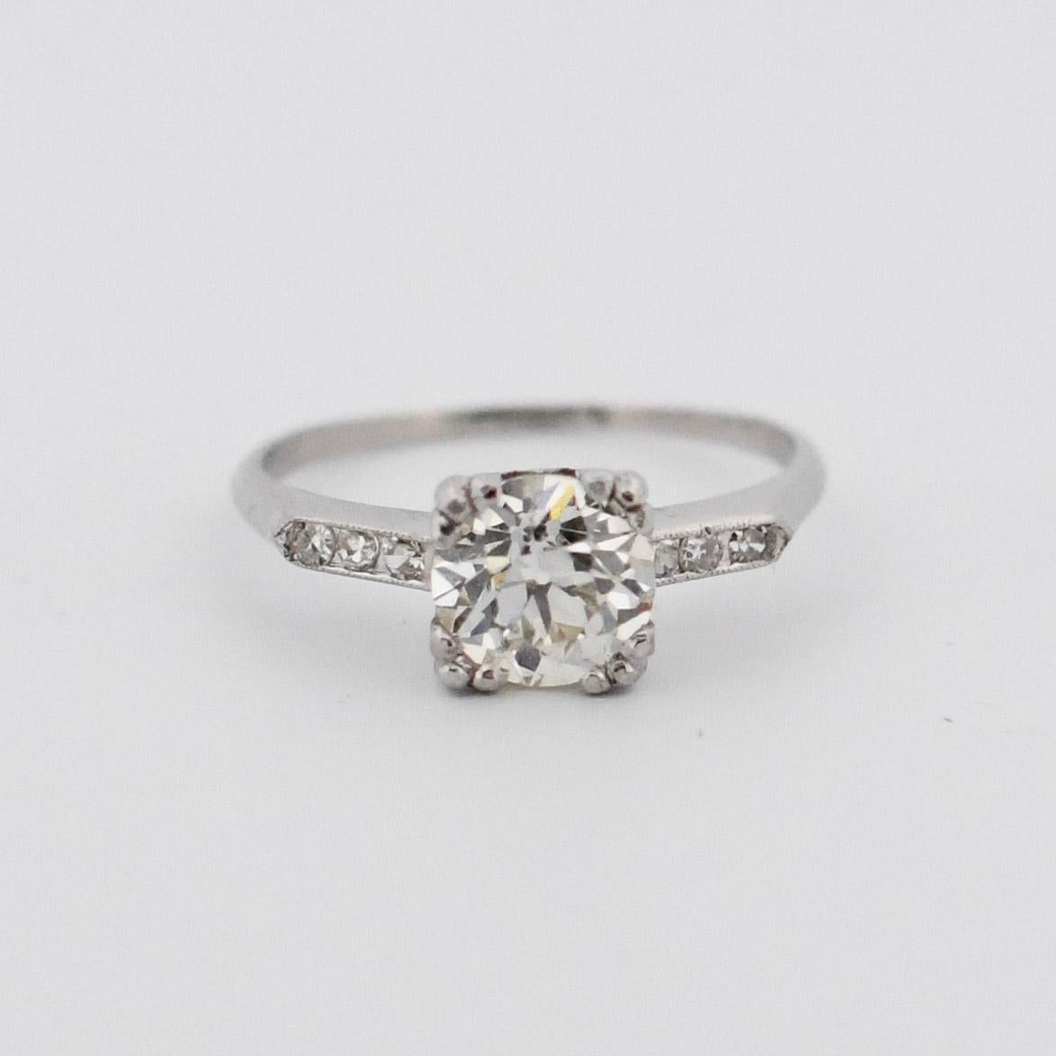 Presented here is a timeless platinum engagement ring in the Art Deco style. The delicate knife-edge band gracefully leads to a symmetrical arrangement of six single-cut diamonds on each side of the central old-cut gem. Encircling each trio of