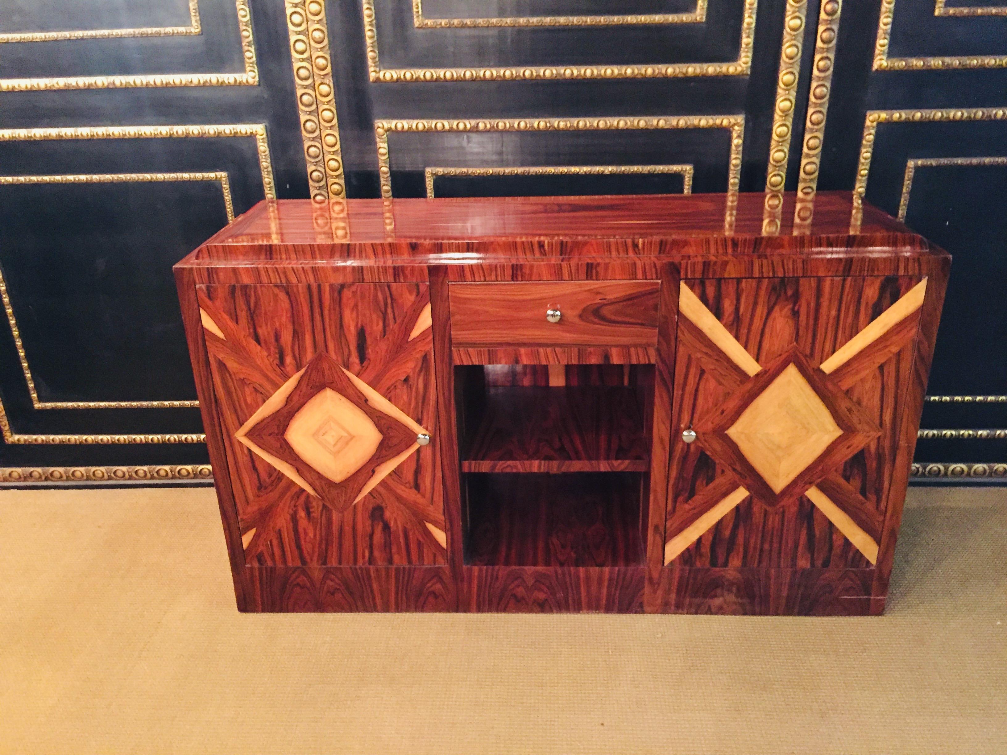 Exotic Indian rosewood on softwood. Rectangular, elongated body on rectangular base plate. In the front center a drawer below open compartment flanked by a double door. Behind each one shelf. Decorative veneer picture.
Beautiful patina, with