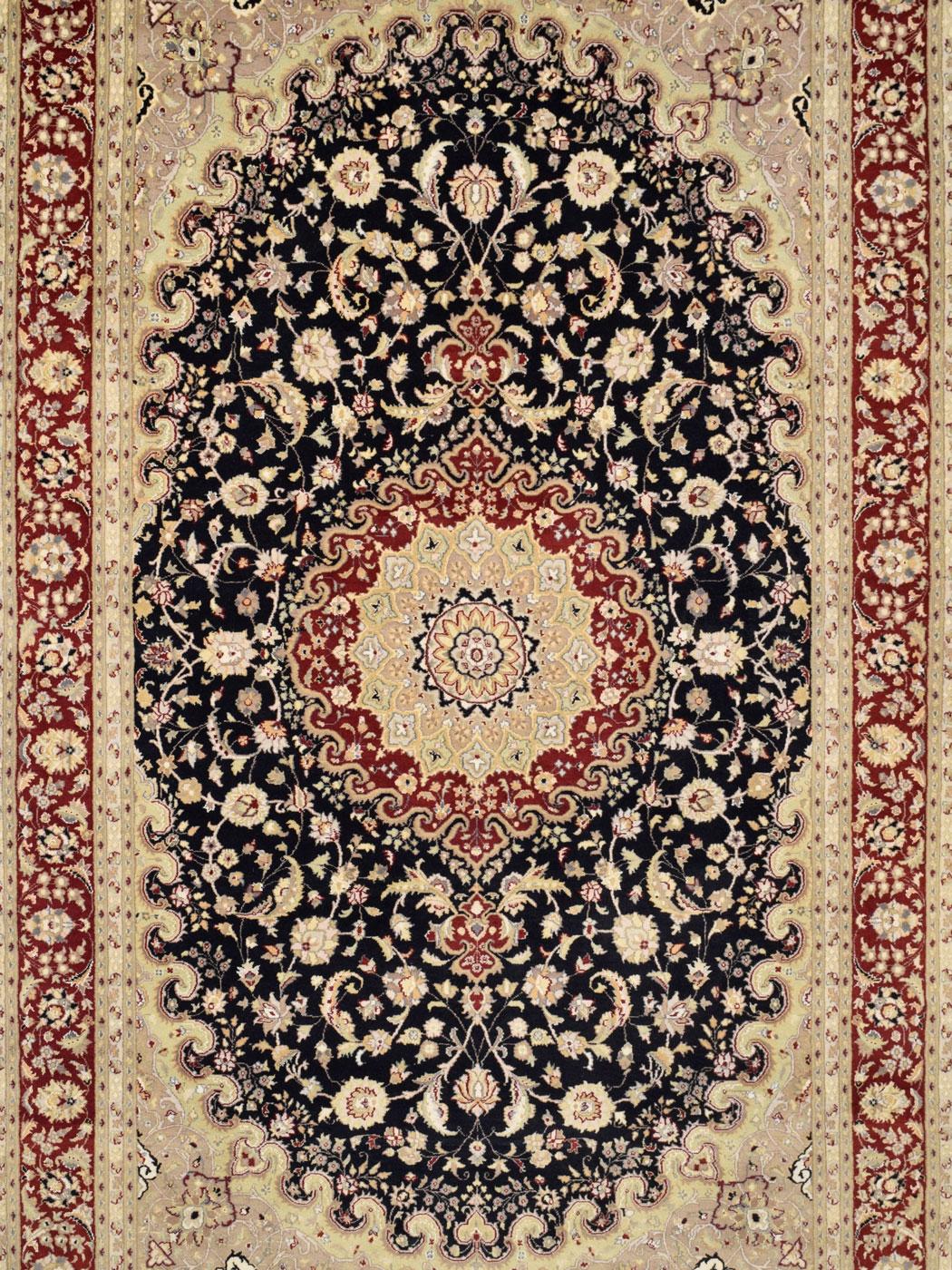 With a dramatic and mesmerizing central medallion, this formal Tabriz carpet measures 6’1”x9’7” and is hand-knotted in black, taupe, red, gold, and cream wool. Woven in Pakistan, this Tabriz design illustrates a flourishing Persian flower garden