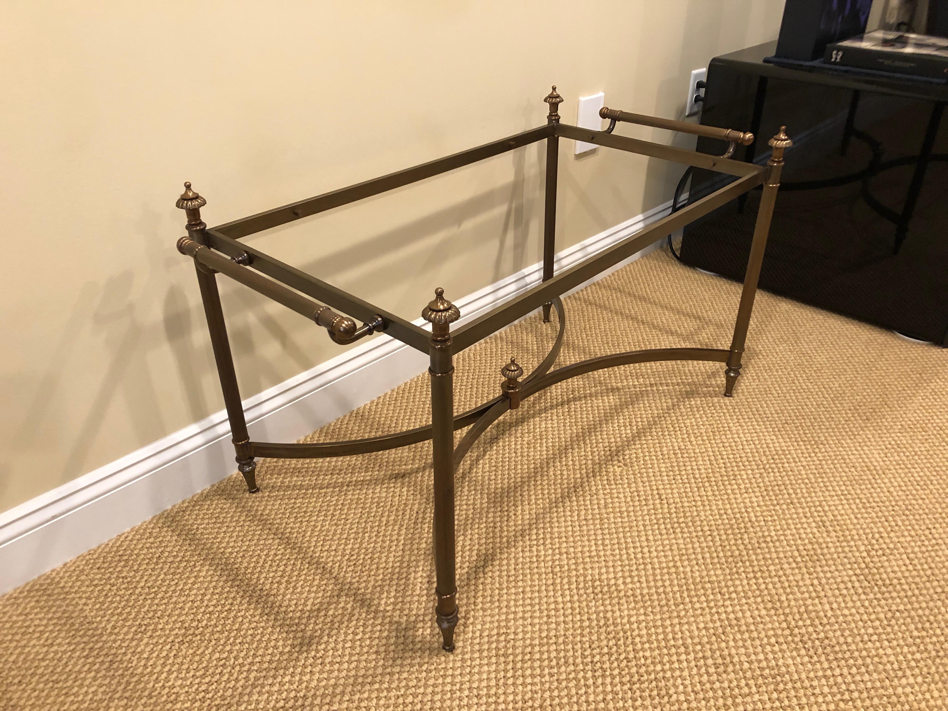 Classically elegant bronze finish coffee table with beveled glass top, having two handles and decorative finials in the corners and underneath in the center of the stretcher bars.
Measures: Height to top of glass is 19.5.