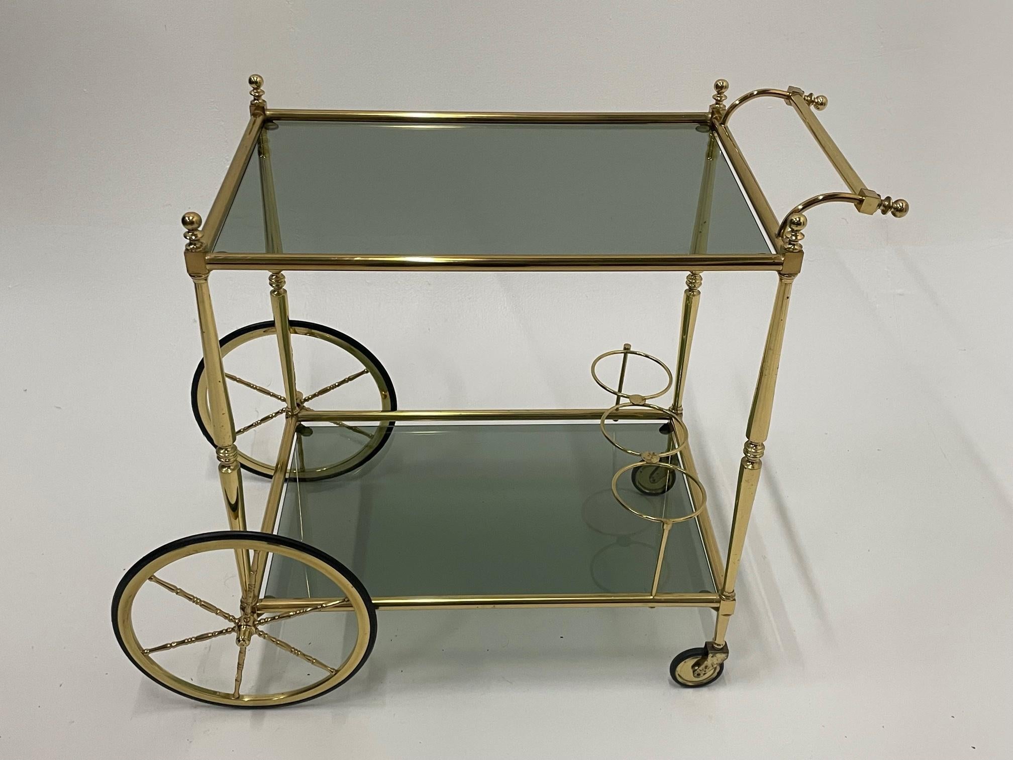 Glamorous and functional Mid-Century Modern brass bar cart having two tiers of smoky glass and a wine rack on the bottom. 27 h to top of handle
Lower tier is 7