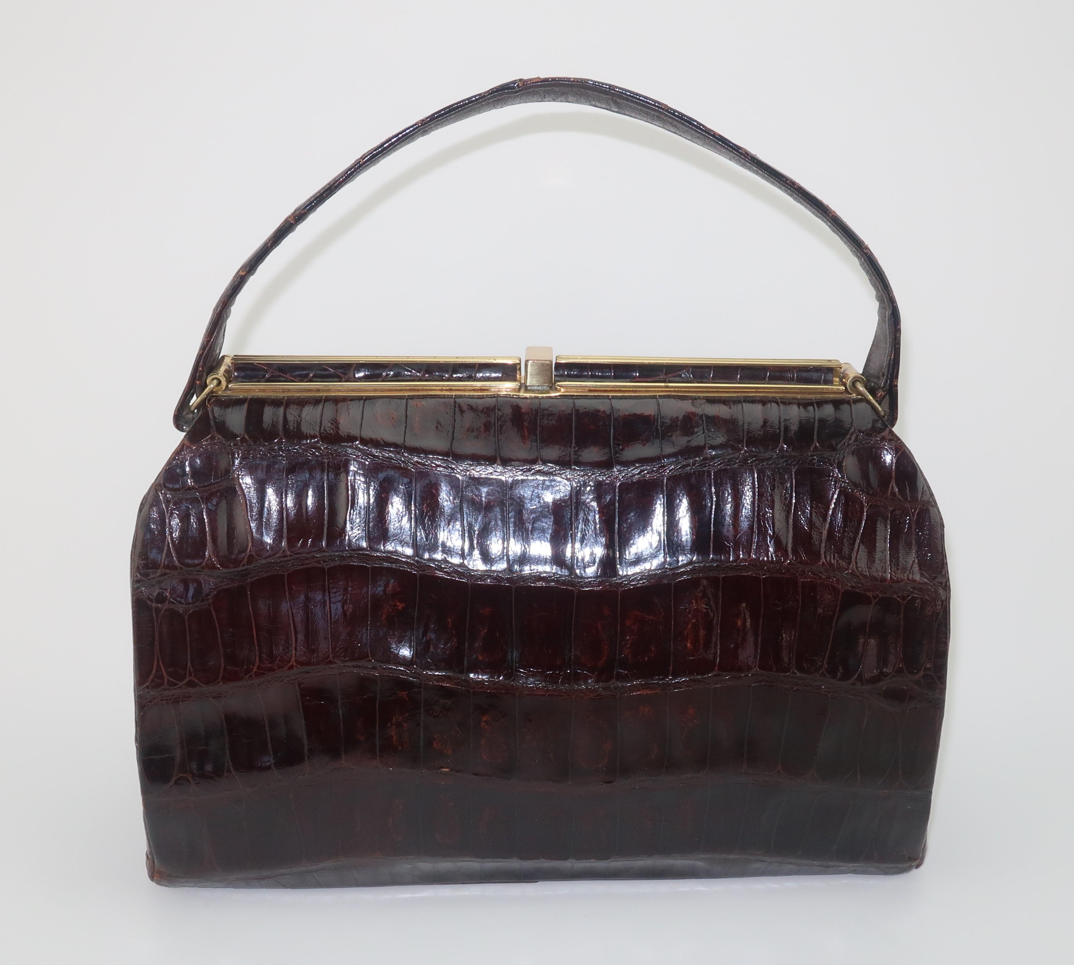 A 1950's classic brown alligator handbag prefect for an Alfred Hitchcock heroine ... think Grace Kelly, Tippi Hedren or Kim Novak. The classic top handle silhouette has a brass frame with a push button that opens to reveal a beige leather lined