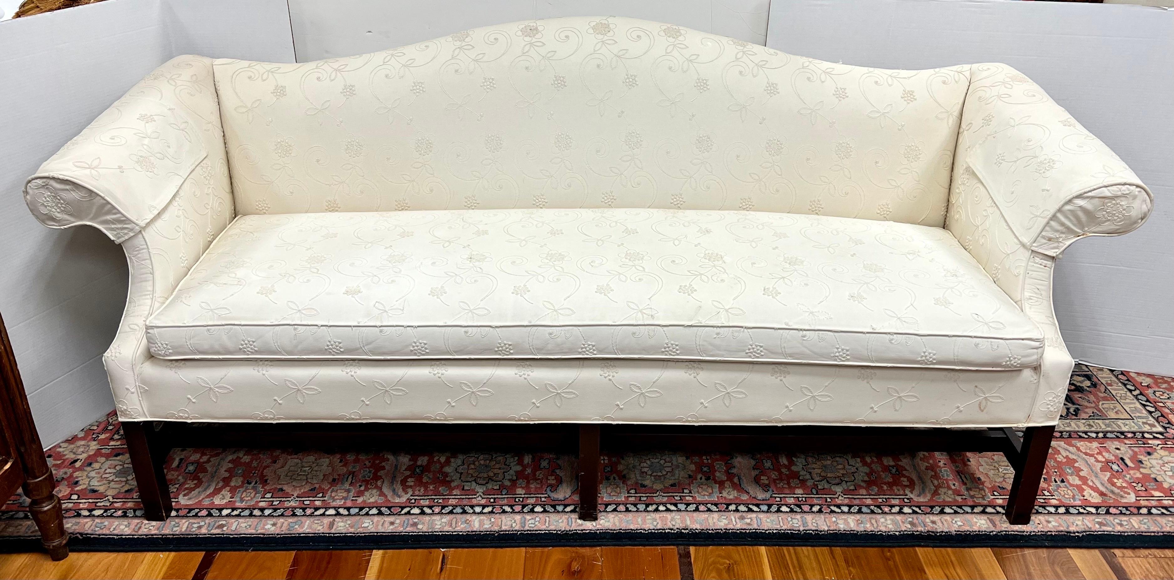 An elegant sofa with Classic and coveted camelback Silhouette and exposed mahogany wood legs and stretcher. Features a stunning off white raised crewelwork fabric and single seat cushion that can fit up to four people. It sits very comfortably. Why