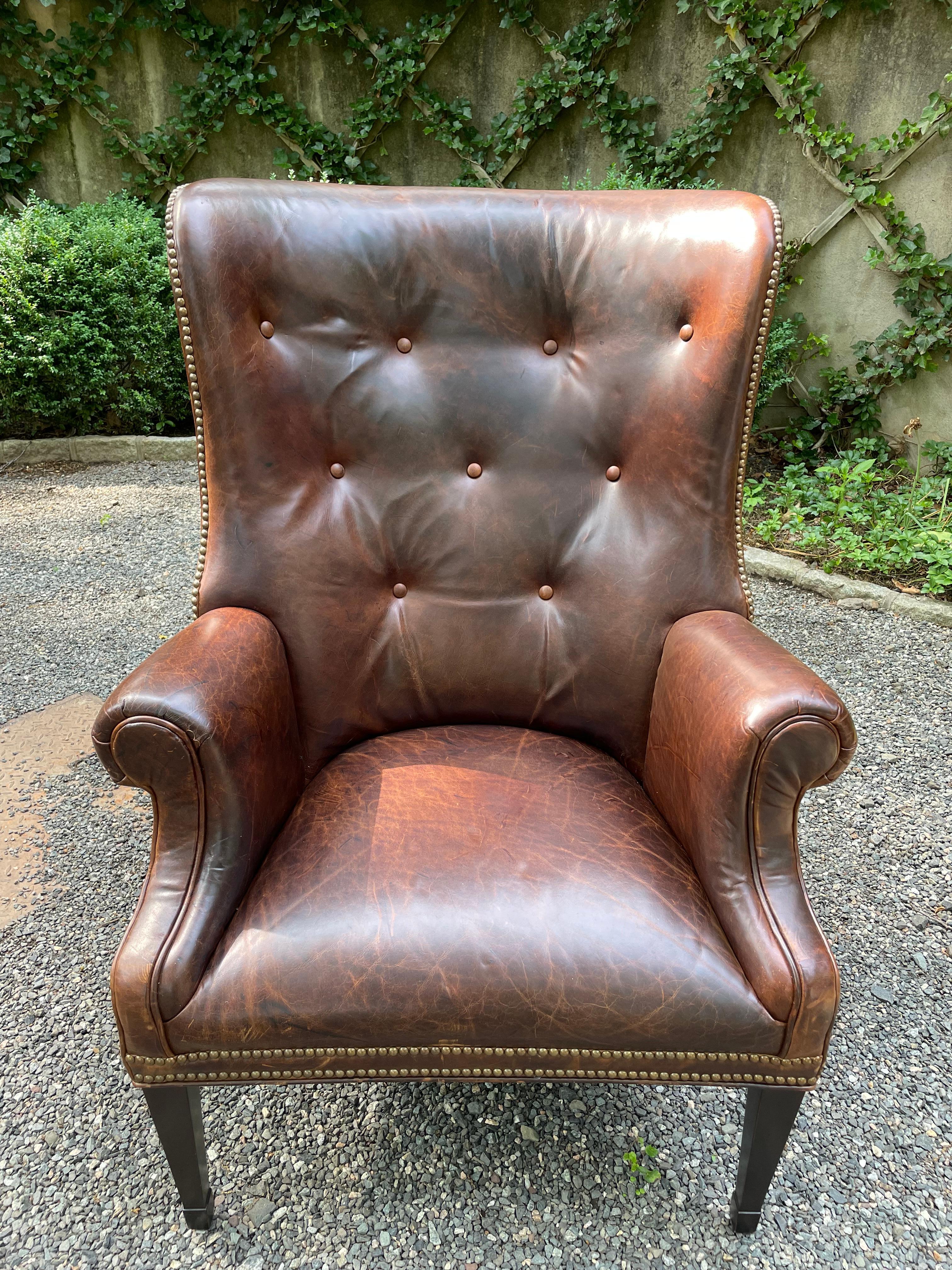 Handsome vintage tufted chocolate brown leather wing chair having nailhead trim around the bottom and mahogany tapered legs.  Arm height 27