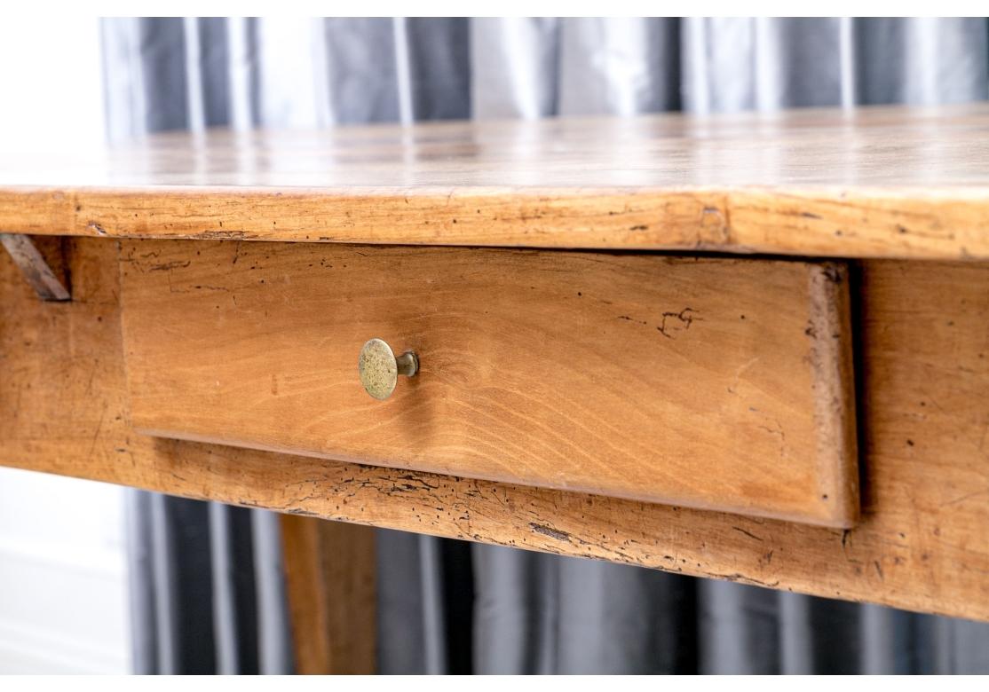 Grazioso tavolo da fattoria francese del XIX secolo dalla forma tradizionale e raffinata. Il piano in legno ammorbidito dal tempo presenta vari segni di usura, tra cui vecchi segni di lavorazione, tarli e bruciature e due utensili.  cassetti (uno
