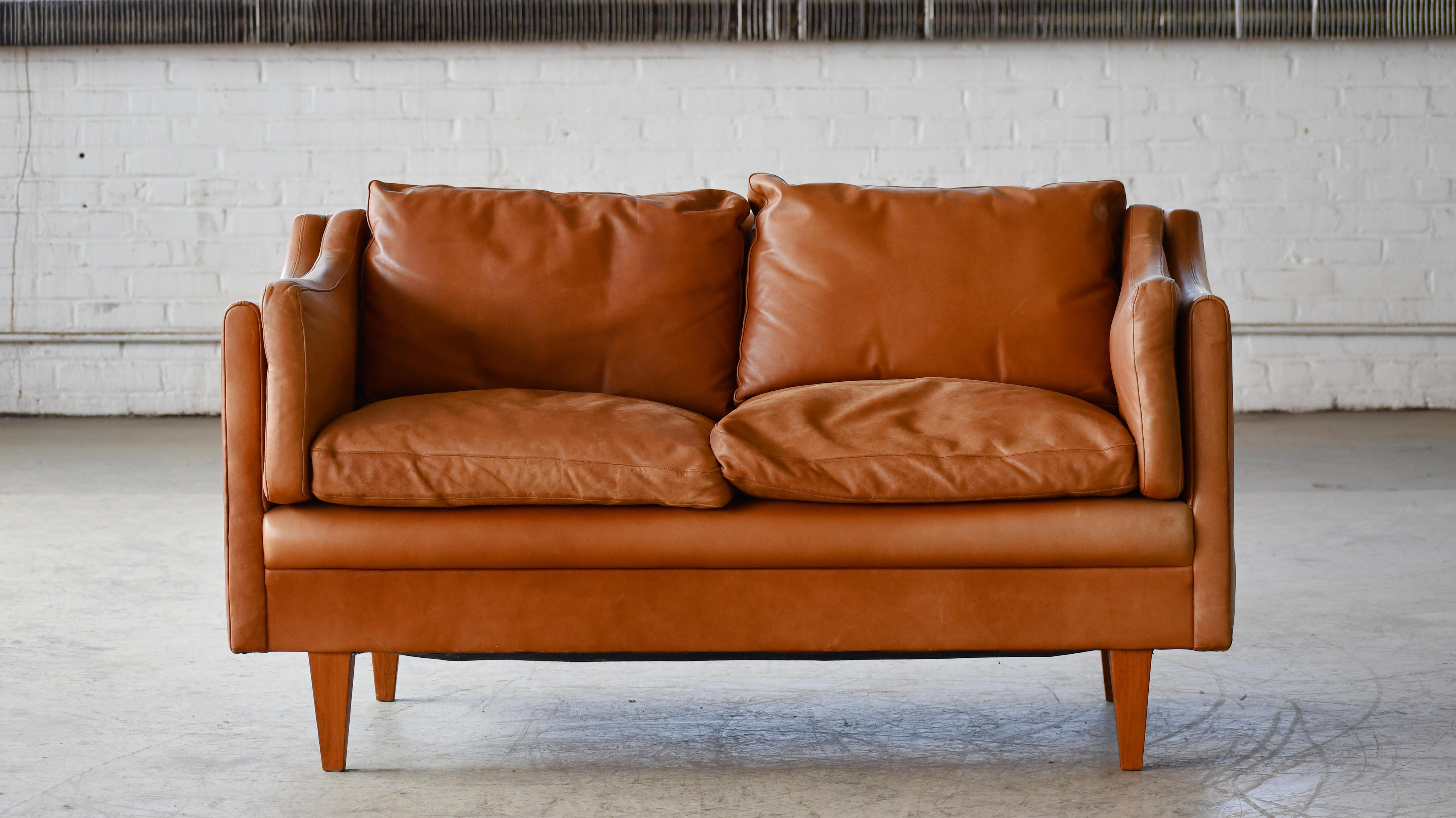 Klassisches dänisches Sofa im Stil von Børge Mogensen in cognacfarbenem Leder. Ganz im Stil von Illum Wikkelso und mit den spitz zulaufenden, abgewinkelten Beinen, die dieser berühmten V-Serie sehr ähnlich sind.   Die mit Daunen gefüllten Kissen