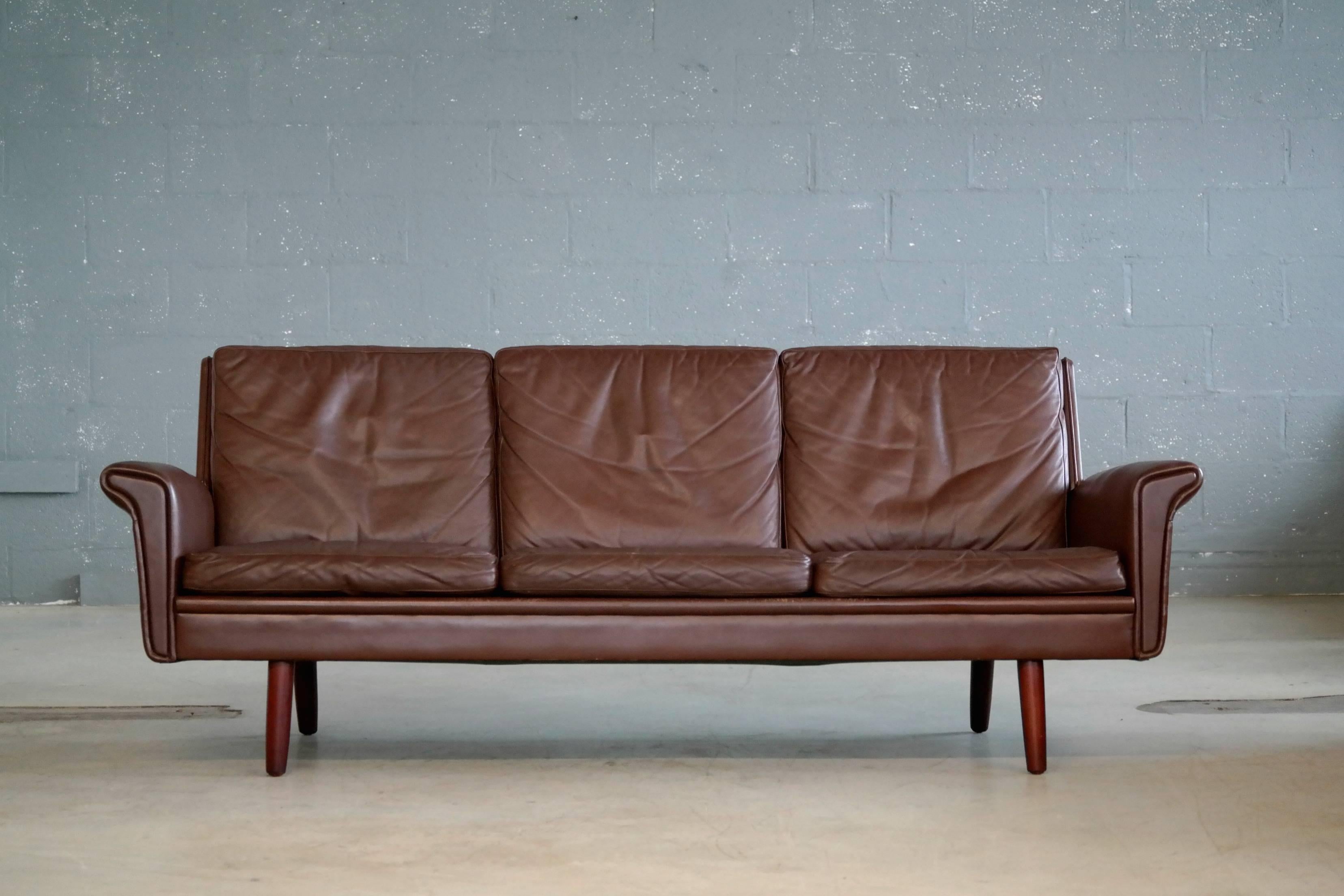 Classic Danish midcentury three-seat leather sofa in a nice warm chestnut color designed by Georg Thams in the late 1960s and manufactured by Vejen Polstermobelfabrik in Denmark. Very elegant with rolled armrests that almost reach out like small