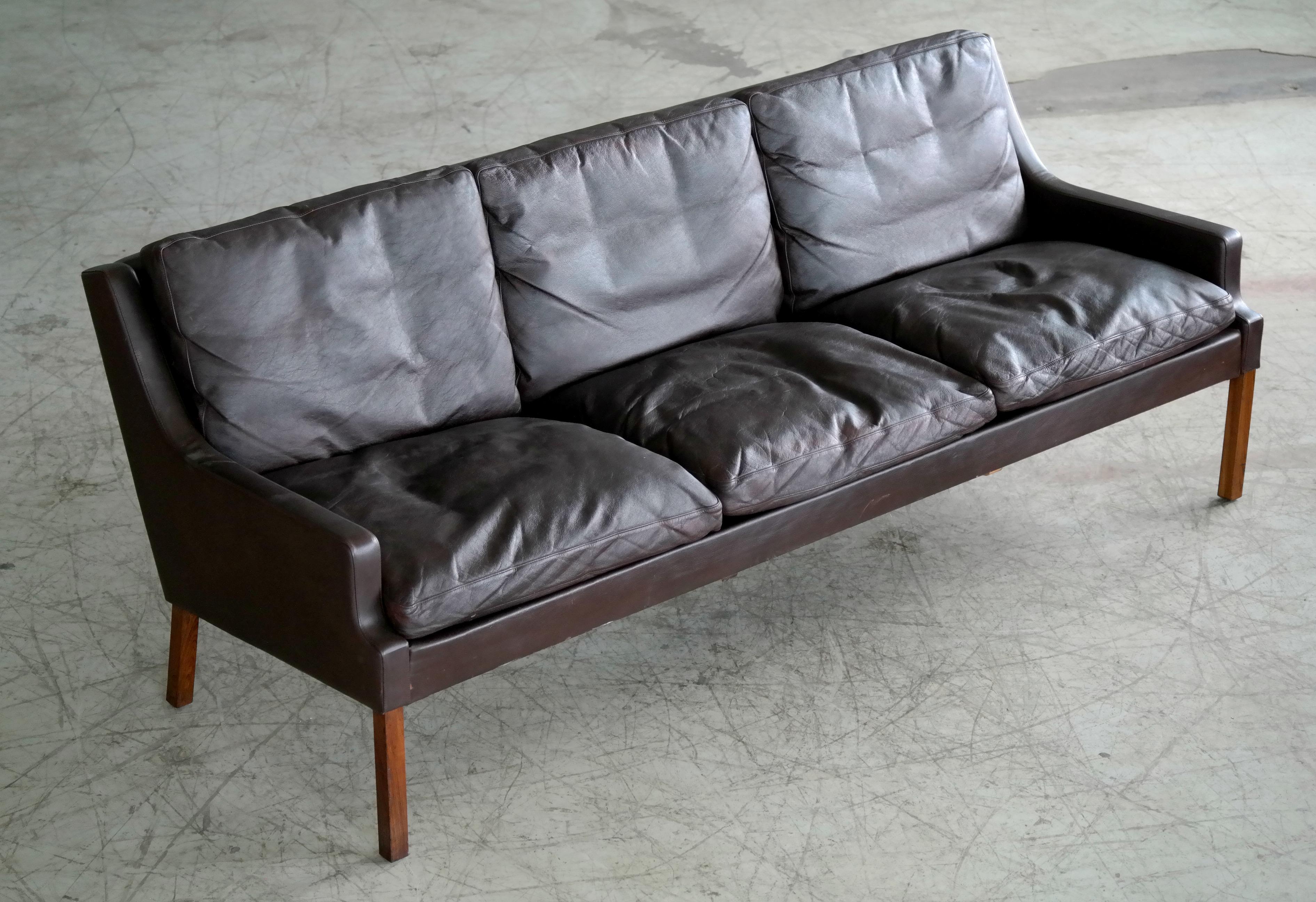 Classic Danish midcentury sofa by Georg Thams from the late 1960s. Slim beautiful silhouette in the style of Hans Olsen's famous designs raised on tall rosewood legs and with down filled cushions wrapped in espresso colored leather. Great patina and