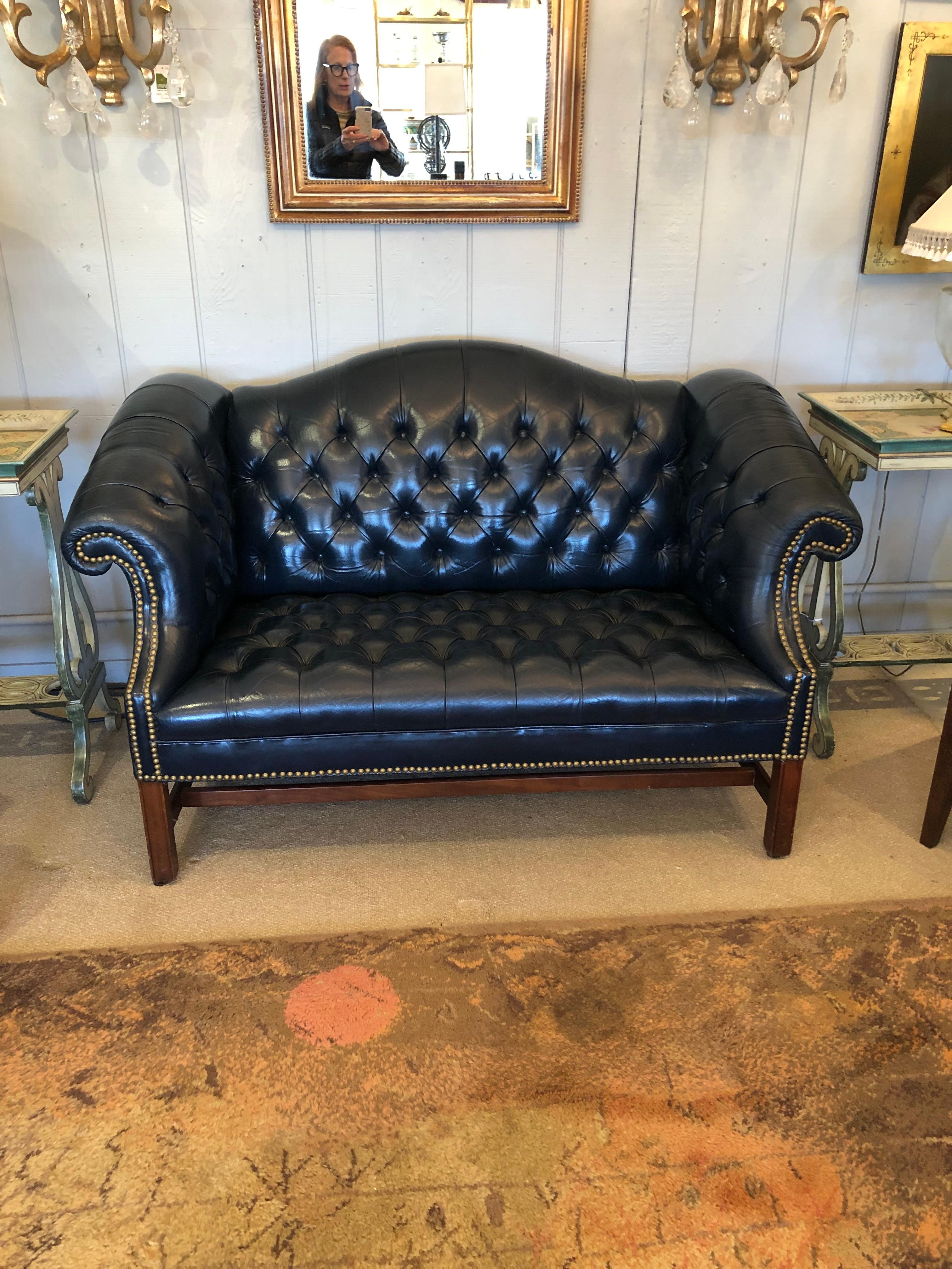 Classic Chesterfield style tufted navy blue leather or leatherette loveseat having scrolled arms, straight mahogany legs and brass nailhead detailing.  Great size and comfortable.