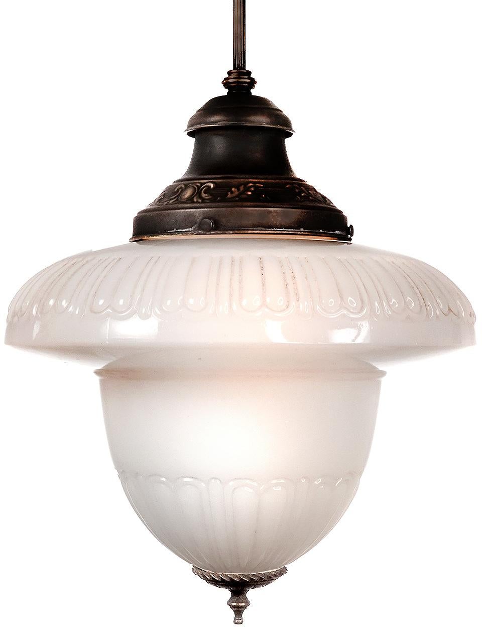 Die Form ist eine überspitzte Eichel aus Milchglas mit geriffelten Bereichen oben und unten. Der originale Schirmhalter hat ein gestempeltes florales Muster. Der Schirm ist außerdem mit einem schönen Zierguss versehen. Ich glaube, der gedrehte Ring