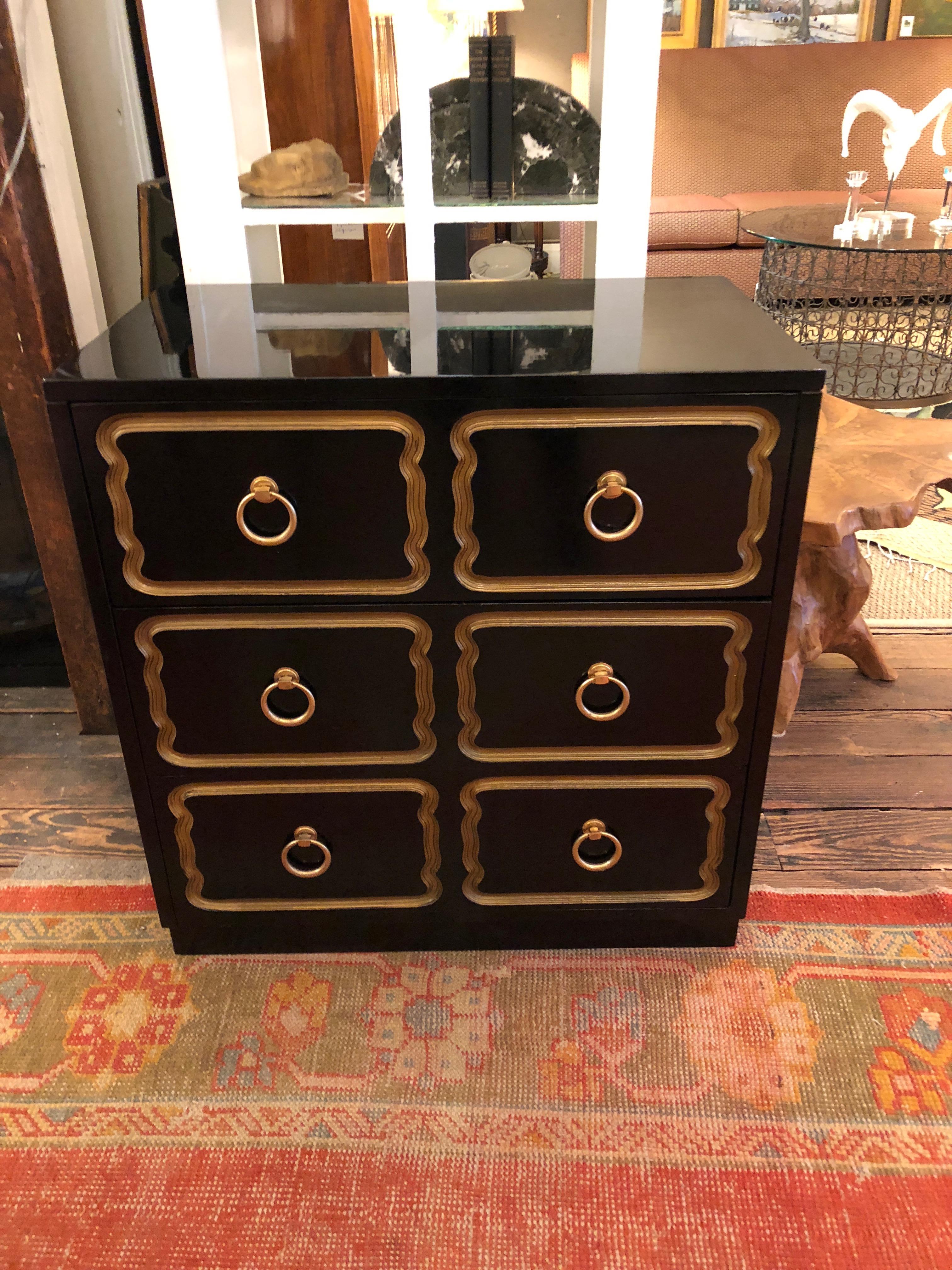 Glamorous black and gold commode with the signature look of a Dorothy Draper design having gold carved squiggly outlines and handsome circular ring hardware on three generously sized drawers.