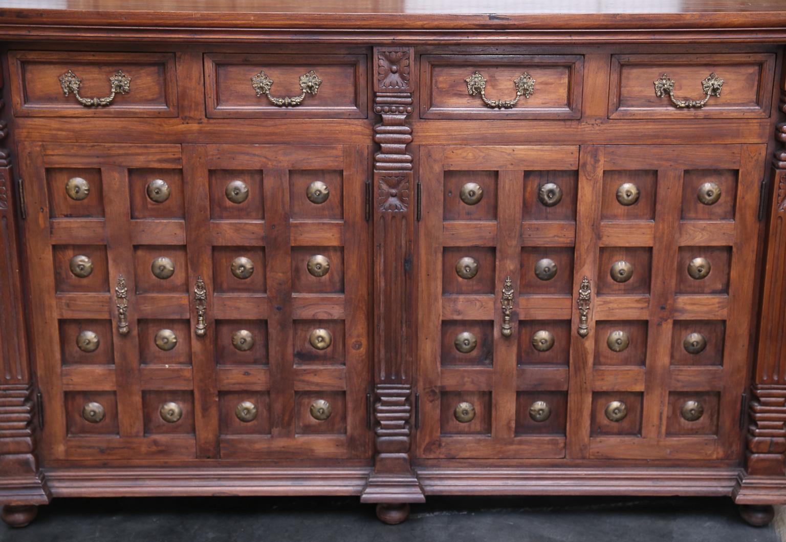 This is a custom made solid teak wood highly decorative side board with metal studs from a French Colonial military officer's home. It has two large bottom shelves with doors and four upper drawers. Handmade solid brass hard wares are used all-over