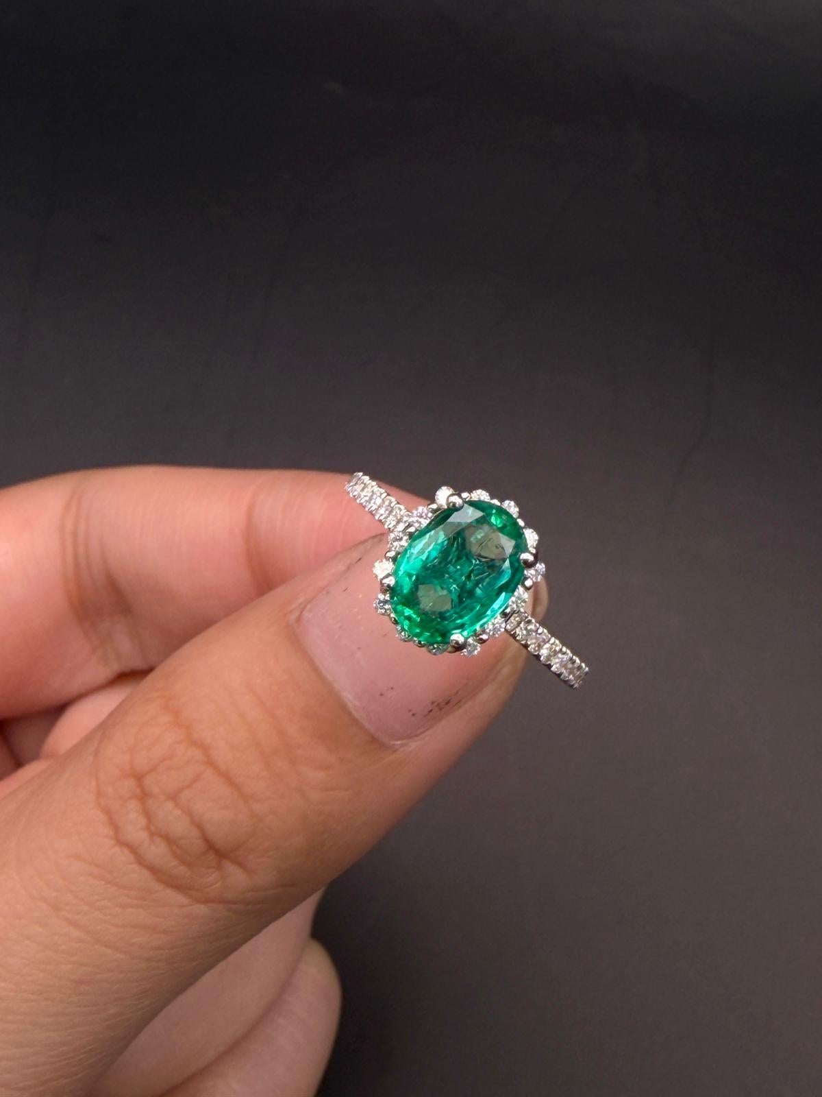 Dieser exquisite Halo-Ring mit Smaragd und Diamant besticht durch einen Smaragd im Ovalschliff mit einem Gewicht von über 1 Karat, der für seine satte grüne Farbe und seine natürliche Tiefe bewundert wird. Das Herzstück ist von einem Halo aus