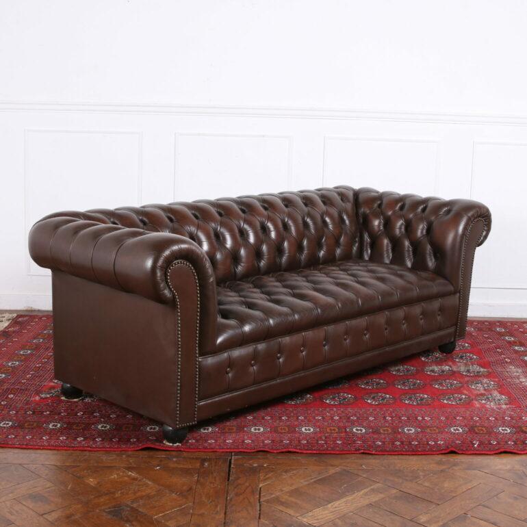 A quality, English, brown leather Chesterfield, with deep button tufting all over and nailhead trim, raised on classic bun feet. Comfortable and in excellent condition. This sofa arrived with a pair of matching leather wing-back chairs 