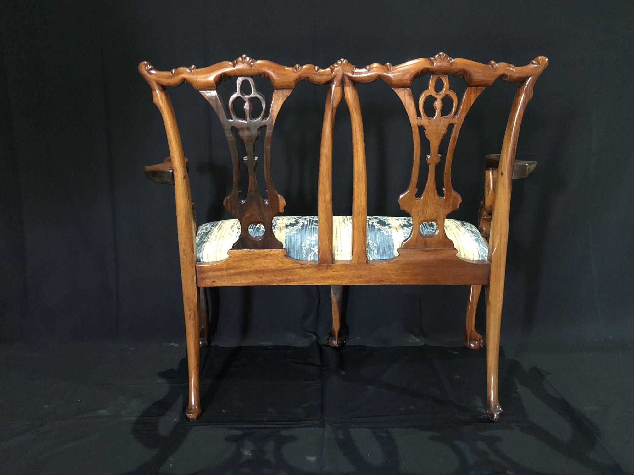 English Chippendale style antique mahogany loveseat with open carved double chair back having cream and blue striped upholstered seat supported on cabriole legs with ball and claw feet. Beautiful carving with sumptuous and immaculate upholstered