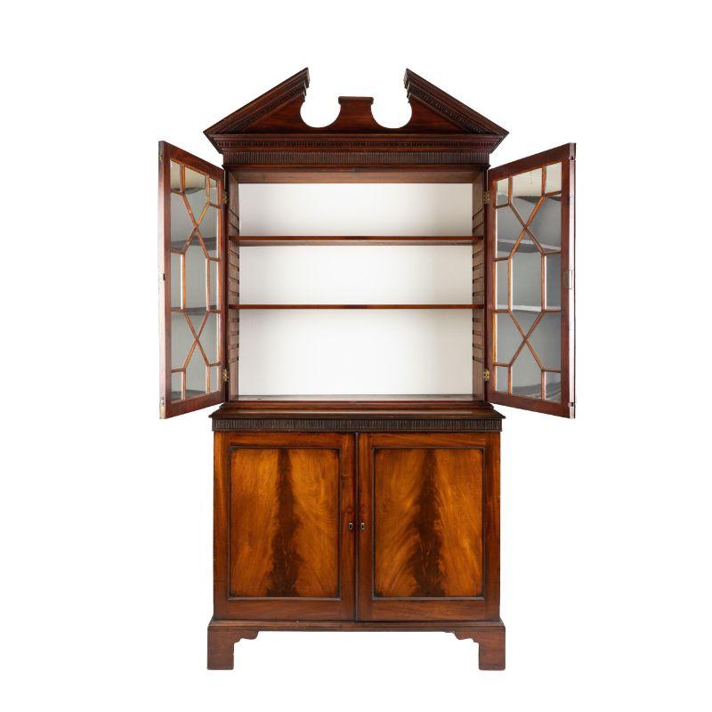 Classic Georgian mahogany bookcase cabinet with astragal mullioned keyed doors. The doors are stepped back over a cabinet with fluted molding above book matched frame and panel, with blind keyed doors. The bookcase is mounted with an entablature in