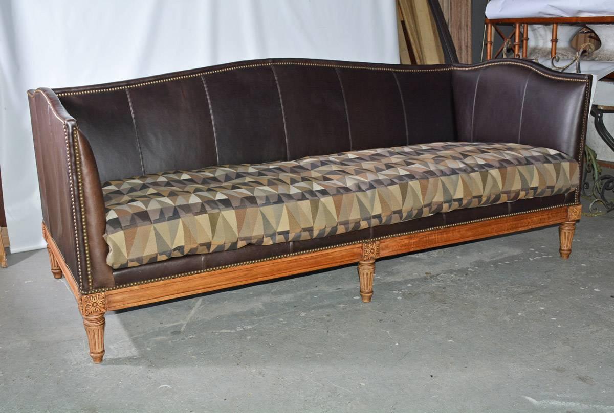 Classic English style sofa upholstered in brown leather with nail heads and camel shape back and sides. One large single cushion covered in complementary geometric design.
    
