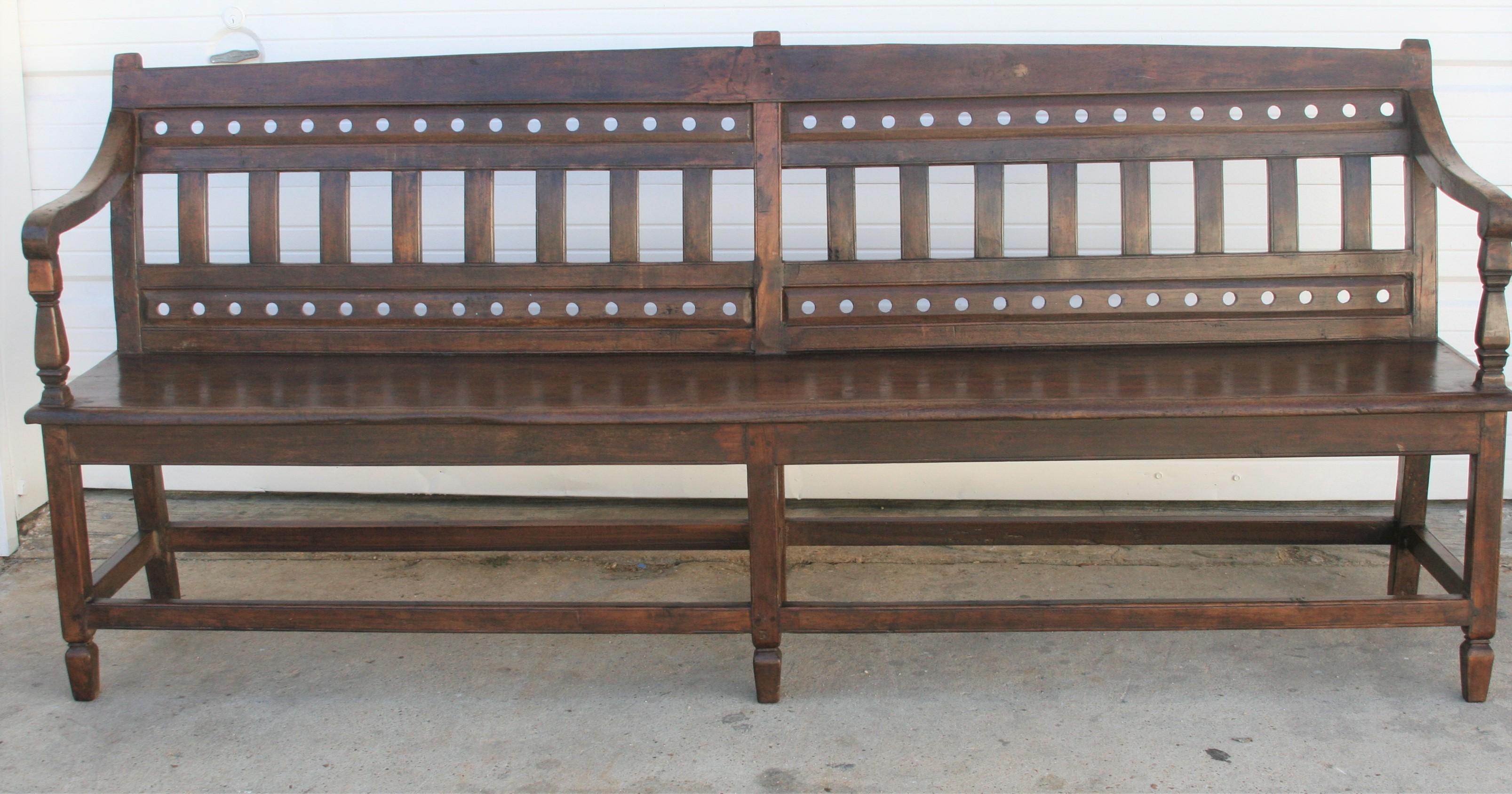 Late 19th century solid teak wood bench from a colonial home. Inimitable in style and unmatched in quality. This long bench has six solid legs with trays holding them and a seat almost made from one plank of wood and arm rests on both sides with