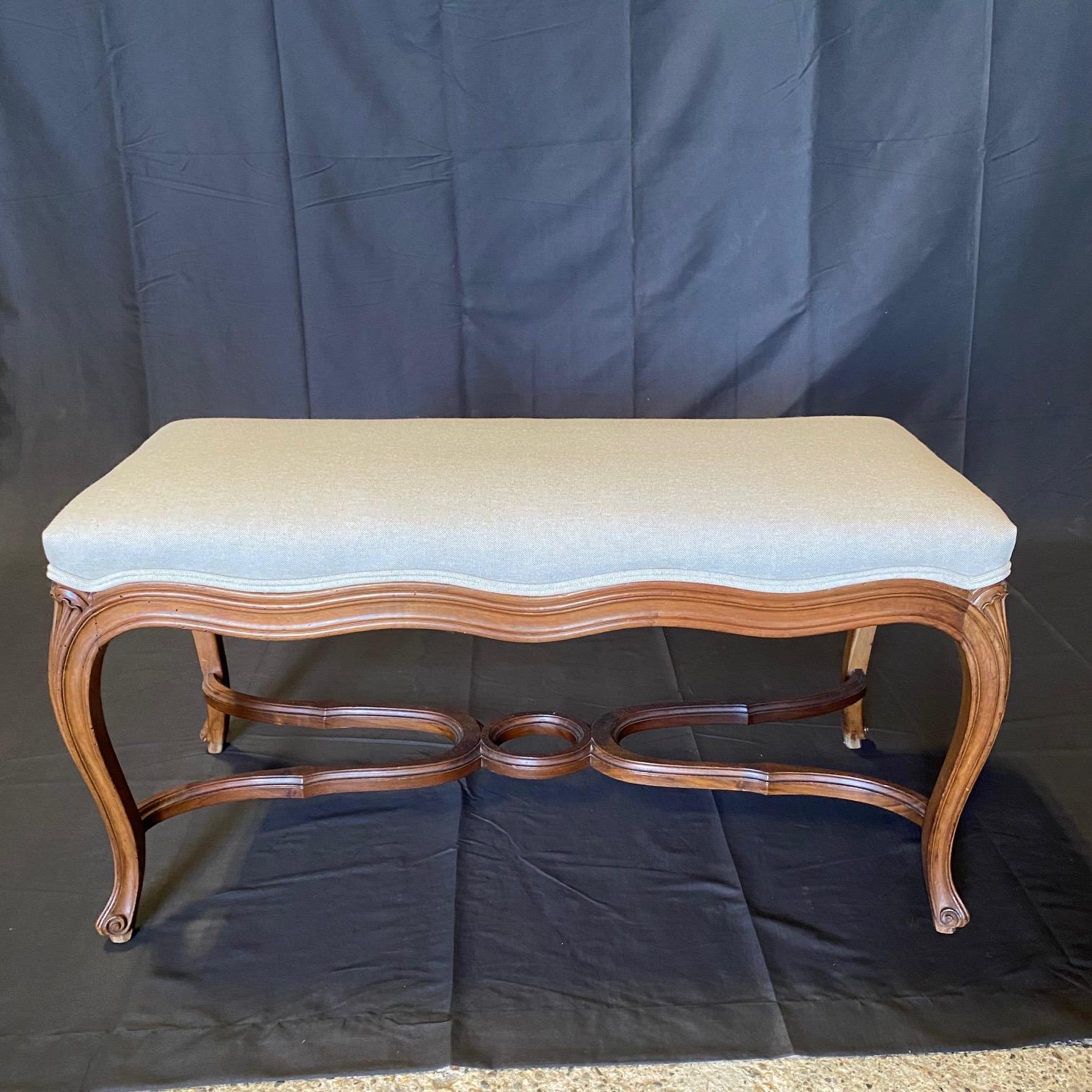 Crafted in France, this elegant antique walnut bench stands on cabriole legs decorated with hand carved acanthus leaf motifs at the shoulder, and ending with escargot feet, over a double curved stretcher with center 