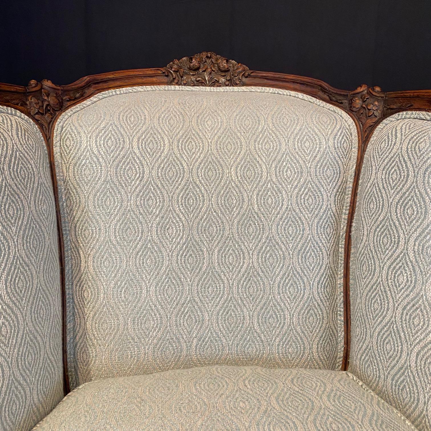 Exquisite detail in the carving on the lovely shaped body of this Louis XV walnut bergere armchair or wingback chair, having carved floral motifs, cabriole legs and new high end upholstery. This classic Louis XV French chair is adorned with
