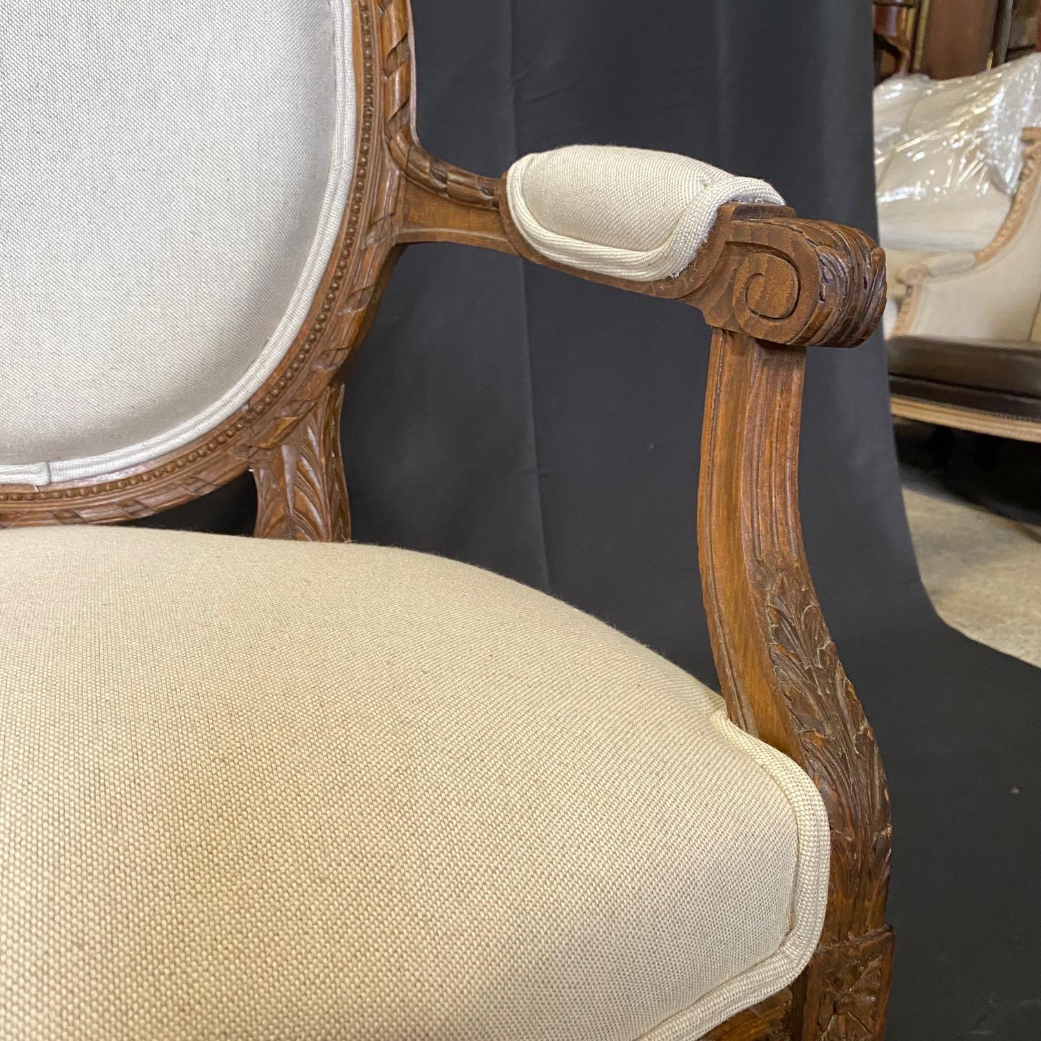 Pair of antique 19th century French Louis XVI armchairs with new neutral high end British upholstery.  Carved beautifully in walnut with a fantastic patina. Each chair is raised by fine and uniquely shaped circular fluted legs below carved block