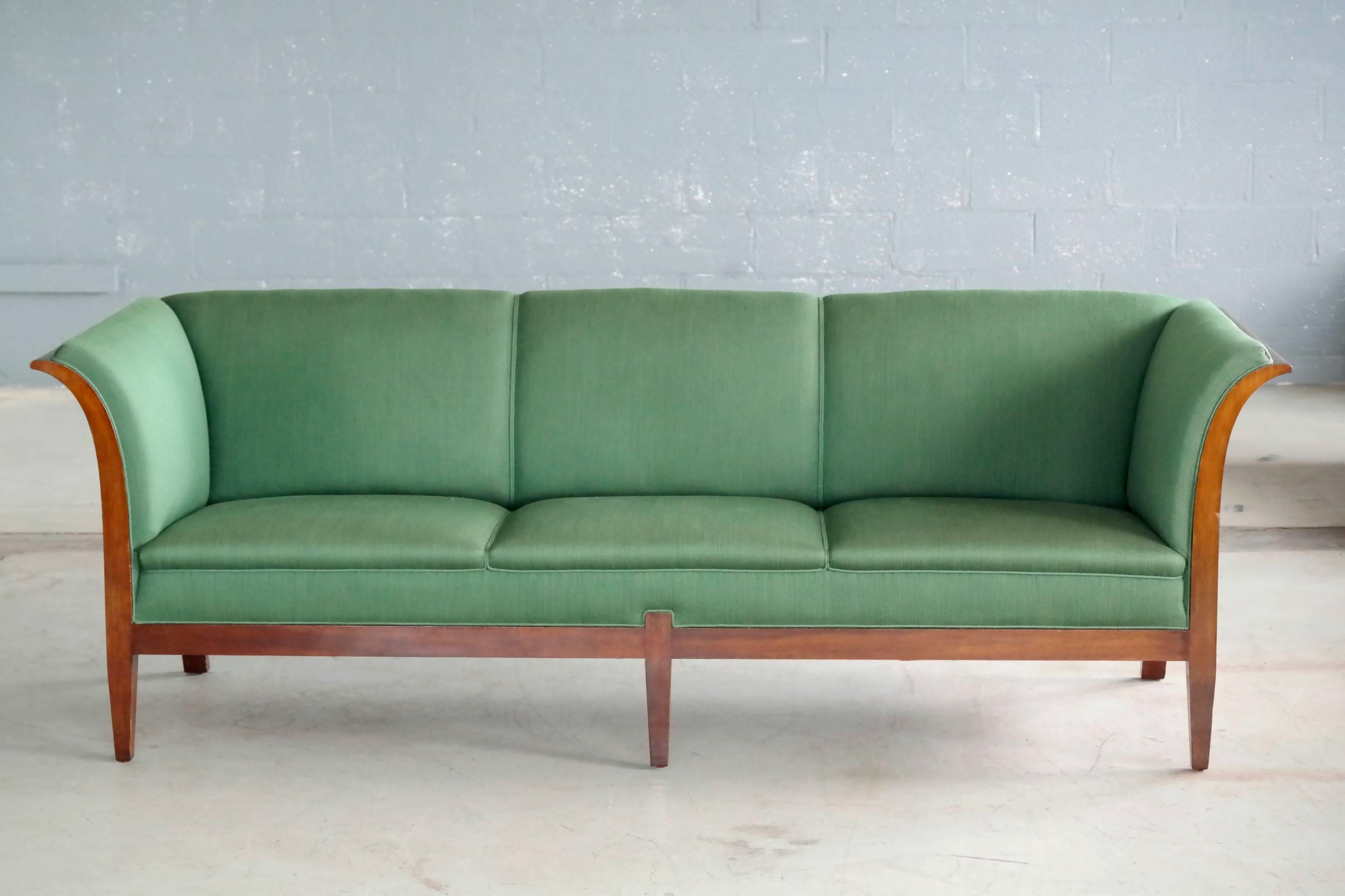 This elegant and generously sized three-seat sofa was designed and made by the Danish Master Cabinetmaker, Frits Henningsen in the 1930s and most likely produced between 1937-1942. The Cuban mahogany frame extends from flared armrests and into a