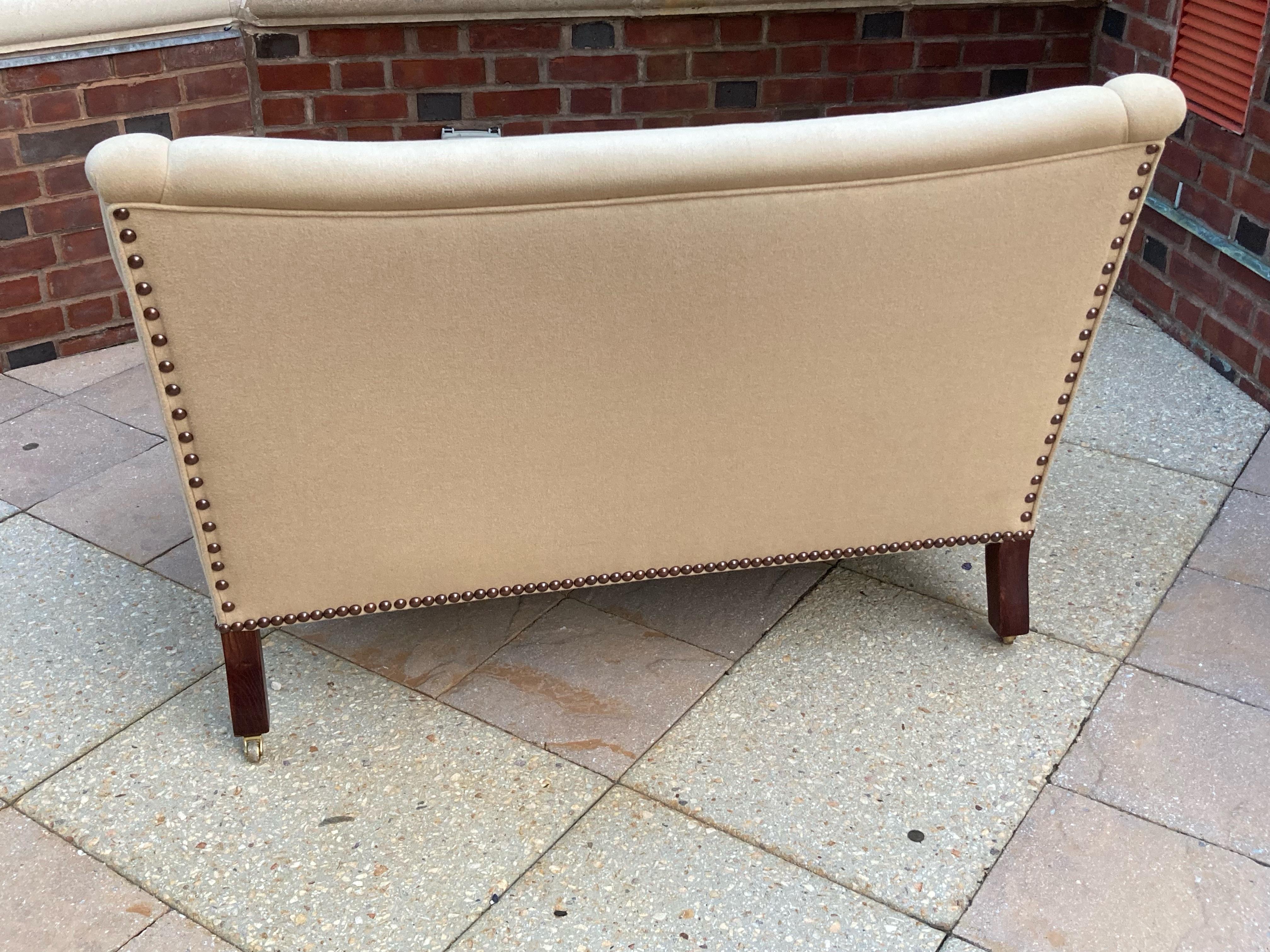 Classic petite Fairhill settee by George Smith having fixed back and fixed seat and upholstered in dark cream wool flannel with handsome nailhead trim and mahogany legs with brass casters. 
There are some spots on upholstery as shown in photos and