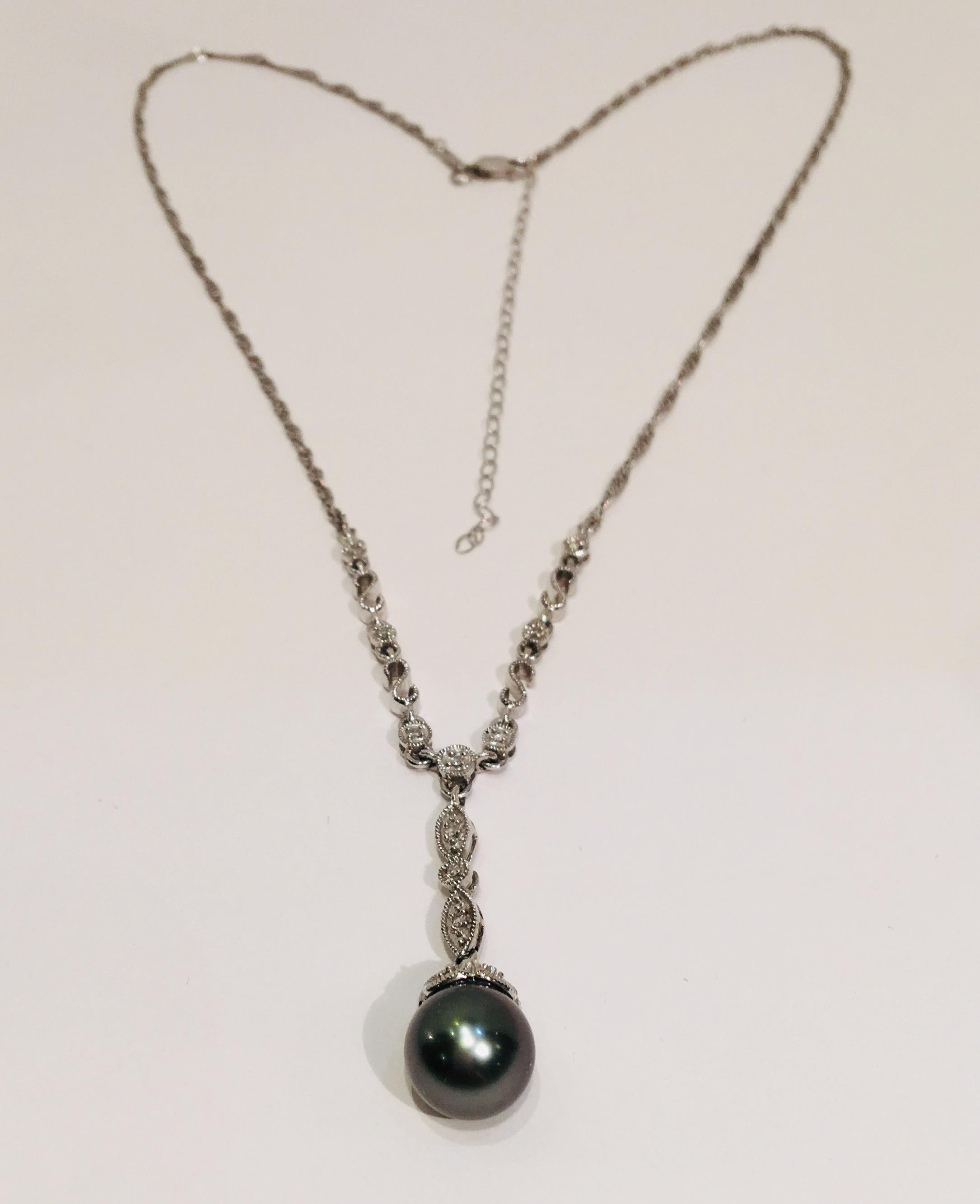 Lovely pendant is a round and lustrous gray Tahitian pearl, mounted in a 14 karat white gold cup which is embellished with fine millgrain details and a pave set diamond.  Pearl is suspended from a solid millgrain station shaped as two marquise