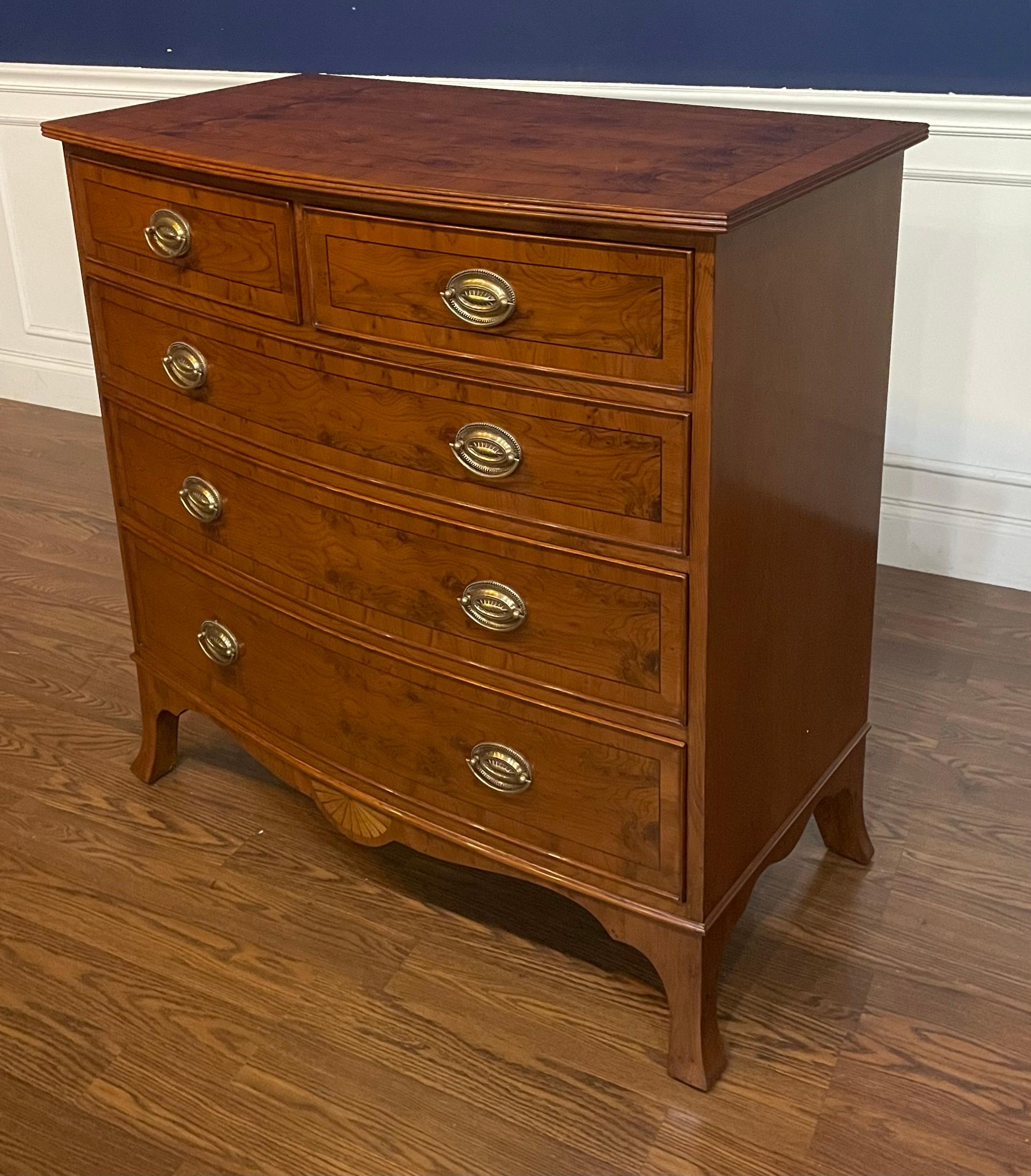 This is a classic Yew wood inlaid bow front chest by Leighton Hall. Its design was inspired by Adams style chests from the early 1800s. It features five drawers, solid brass hardware and faux key holes. The drawer fronts and top have Yew wood with