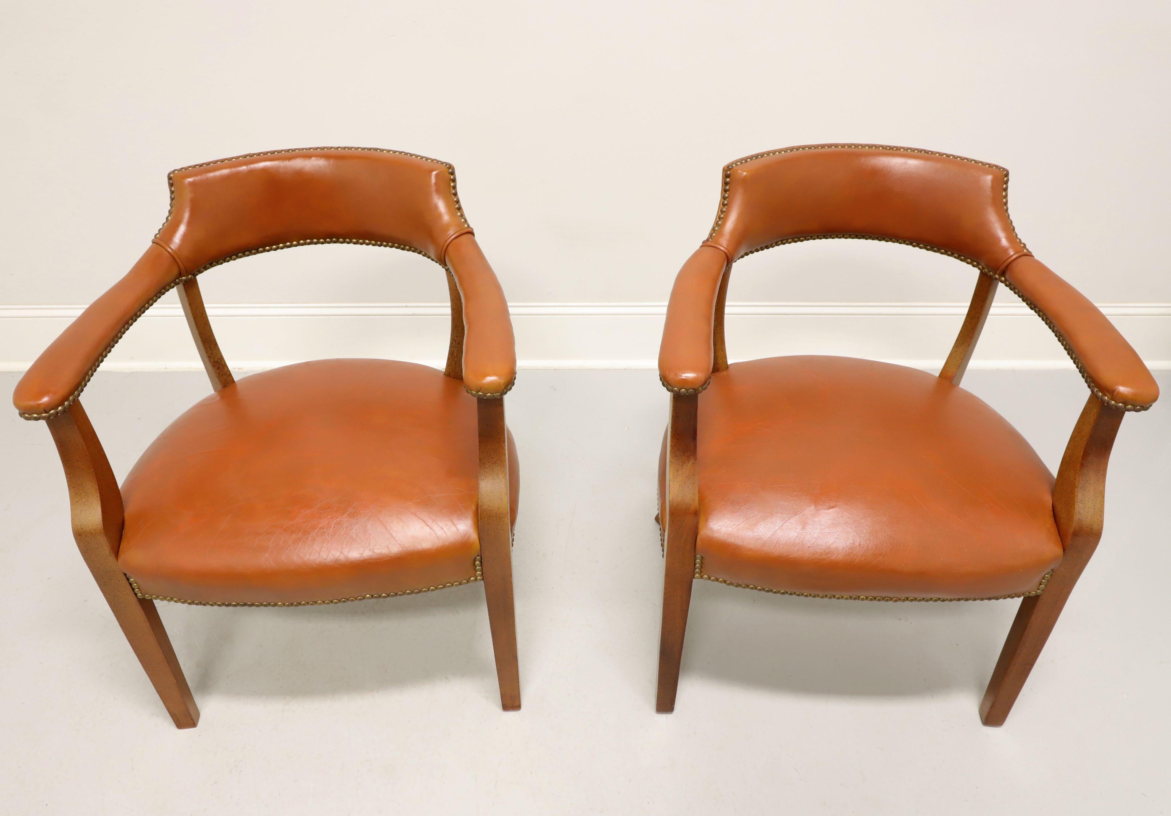 A pair of Traditional style game chairs by Classic Leather. Walnut frame with a distressed finish, light brown color leather upholstered, barrel back, brass nailhead trim, flared rear legs and straight front legs. Made in Conover, North Carolina,