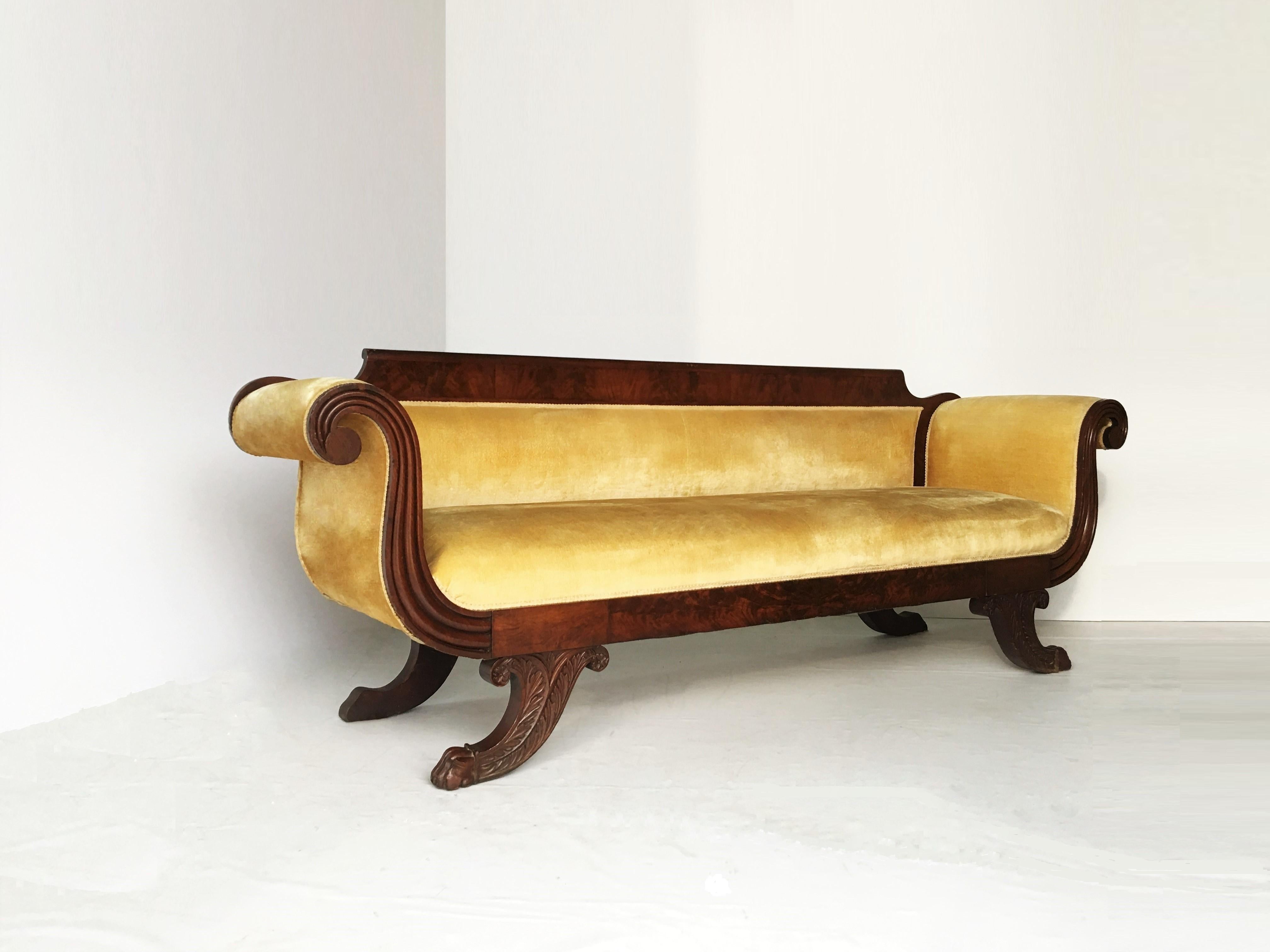 Classical upholstered in yellow velvet carved mahogany Grecian sofa, probably New York. With highly figured mahogany veneers on carved crest rail and front seat rail terminating at each arm scrolled. Floral carved saber shaped legs ending in paw