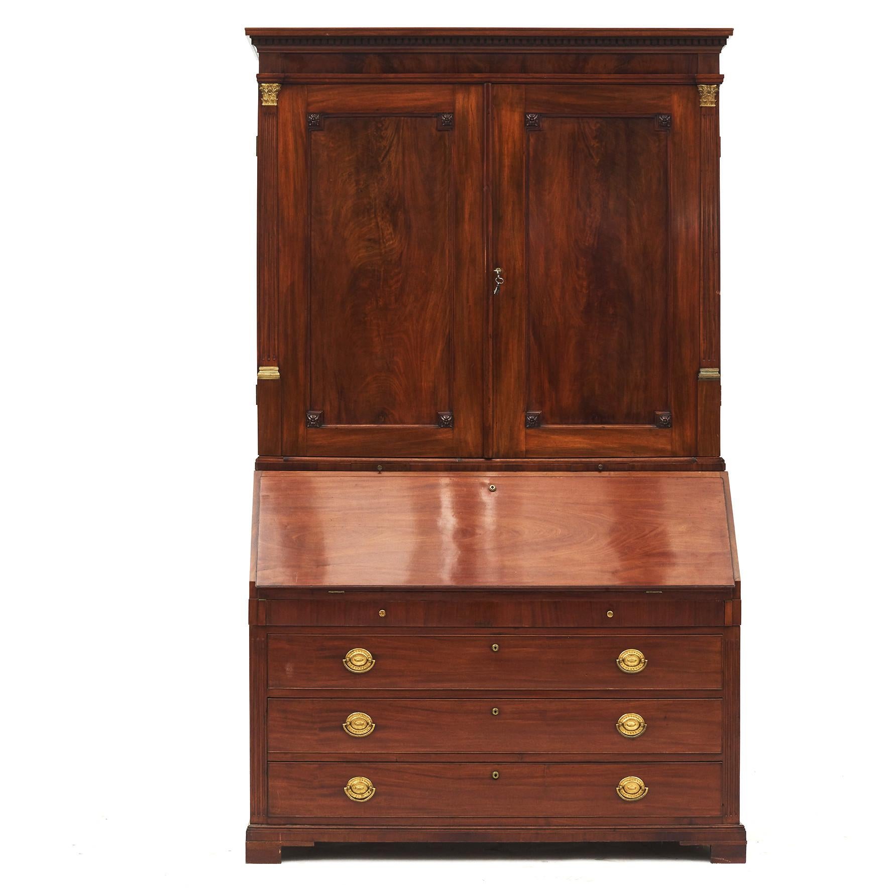 Late 18th-early 19th century mahogany bureau bookcase in the George III manner.
Upper section with dentil crown moulding supported over two doors flanked by fluted pilasters with brass capitals.
Lower section with three large drawers below a small