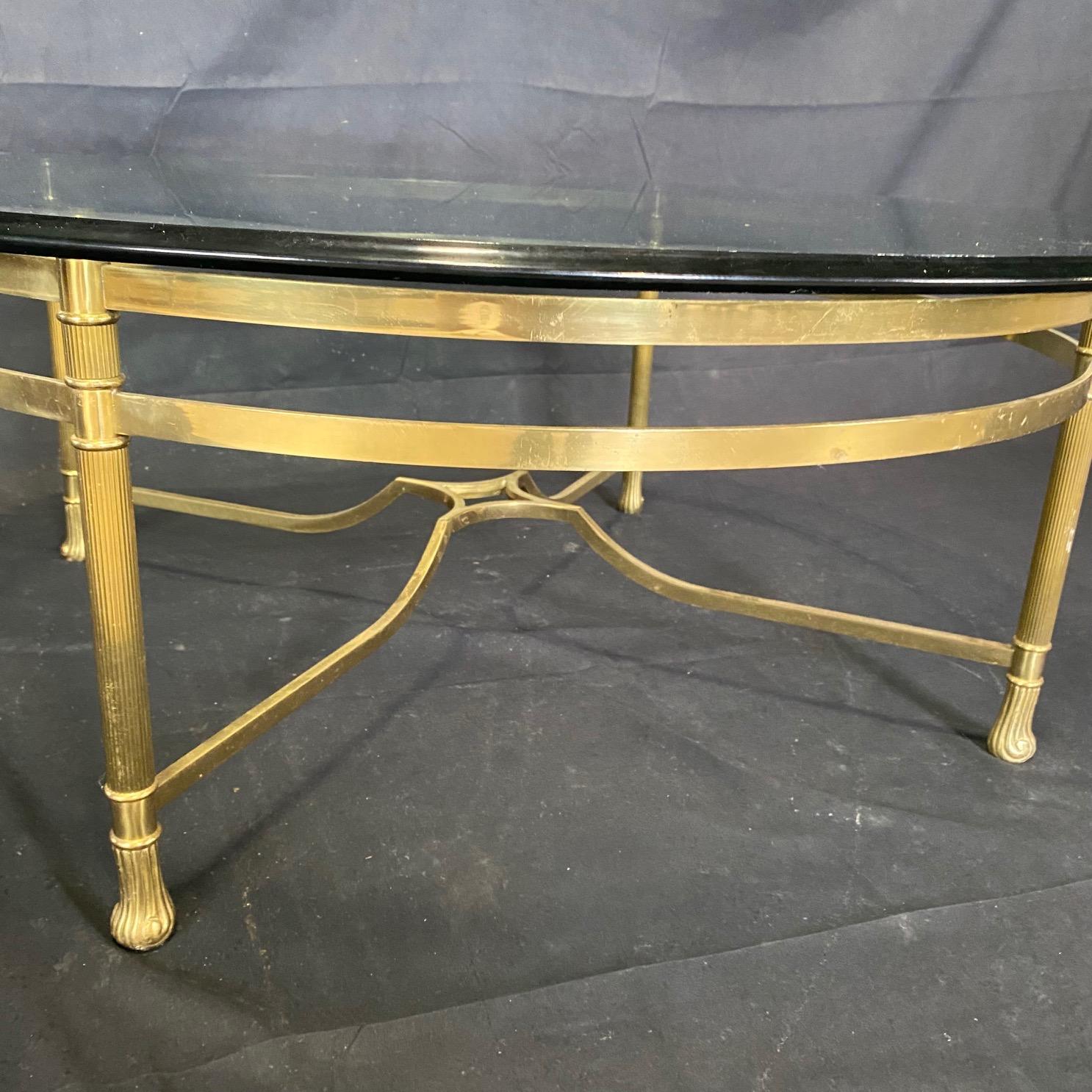A classic brass and glass cocktail table by Labarge having solid brass curvy base with cabriole legs and pretty stretcher, topped with a thick scalloped carved edge piece of round glass.

